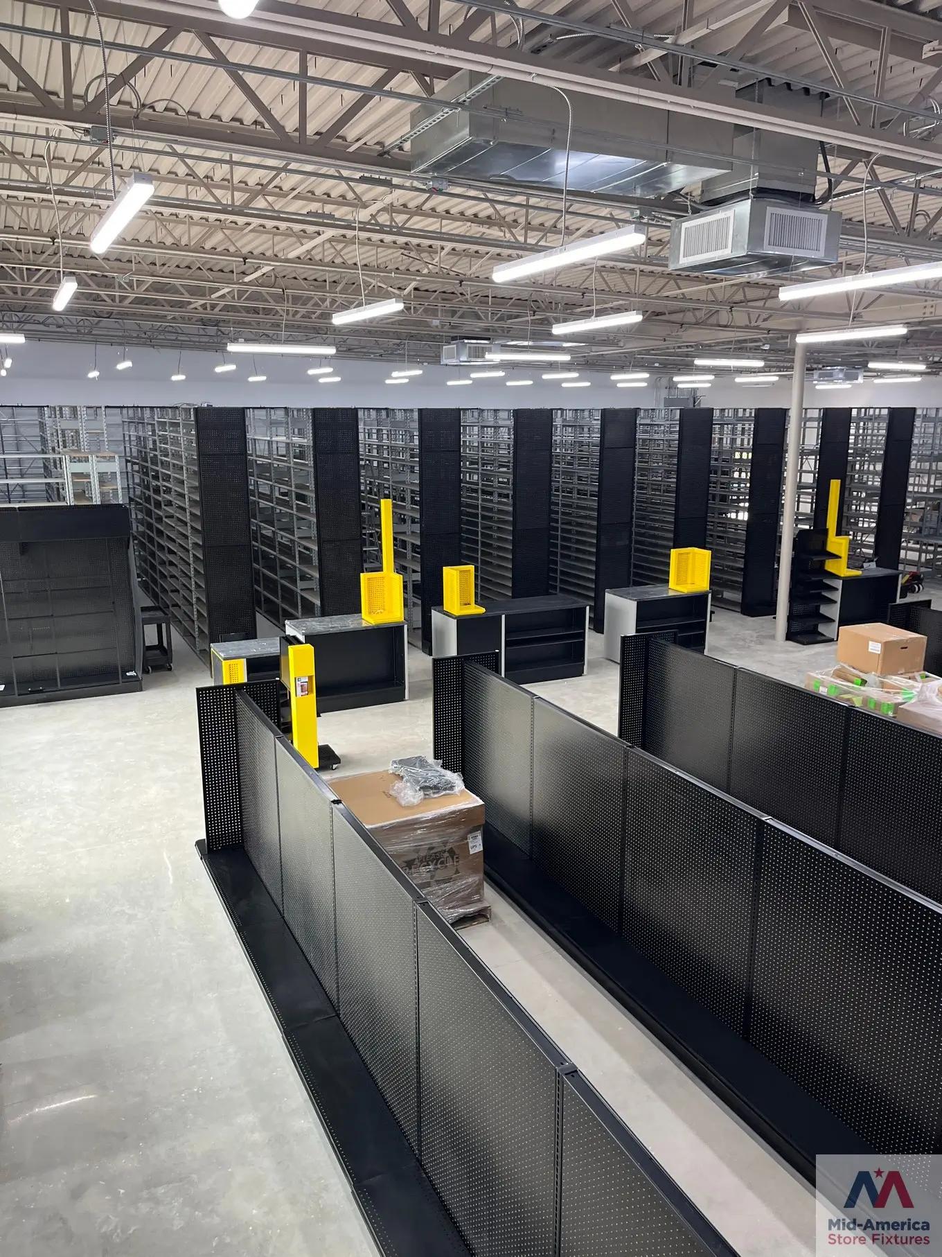 A retail warehouse space with rows of black gondola shelving units, overhead lighting, and a visible ceiling structure.