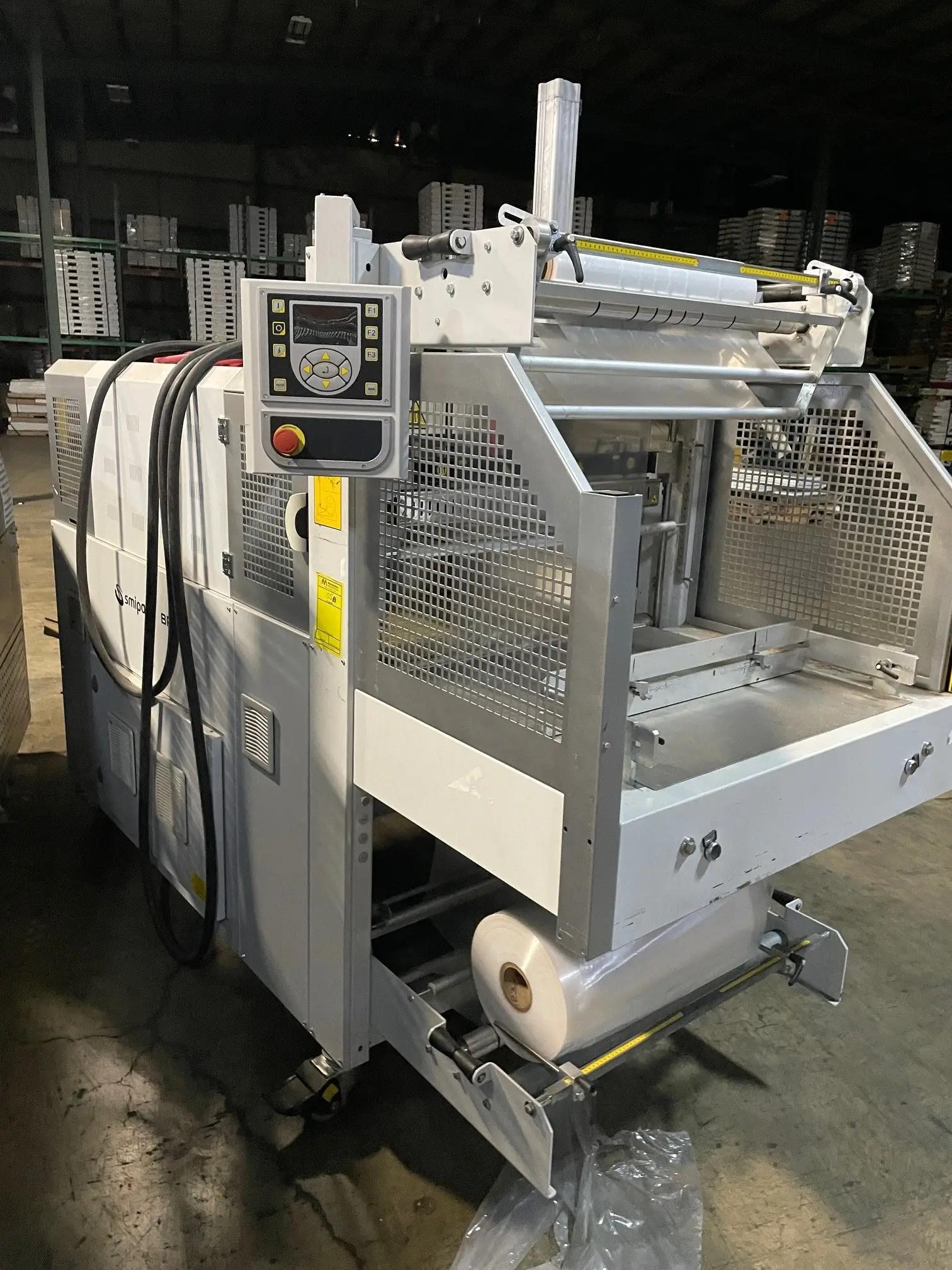 An industrial packaging machine with a control panel and a roll of plastic film in a warehouse setting.