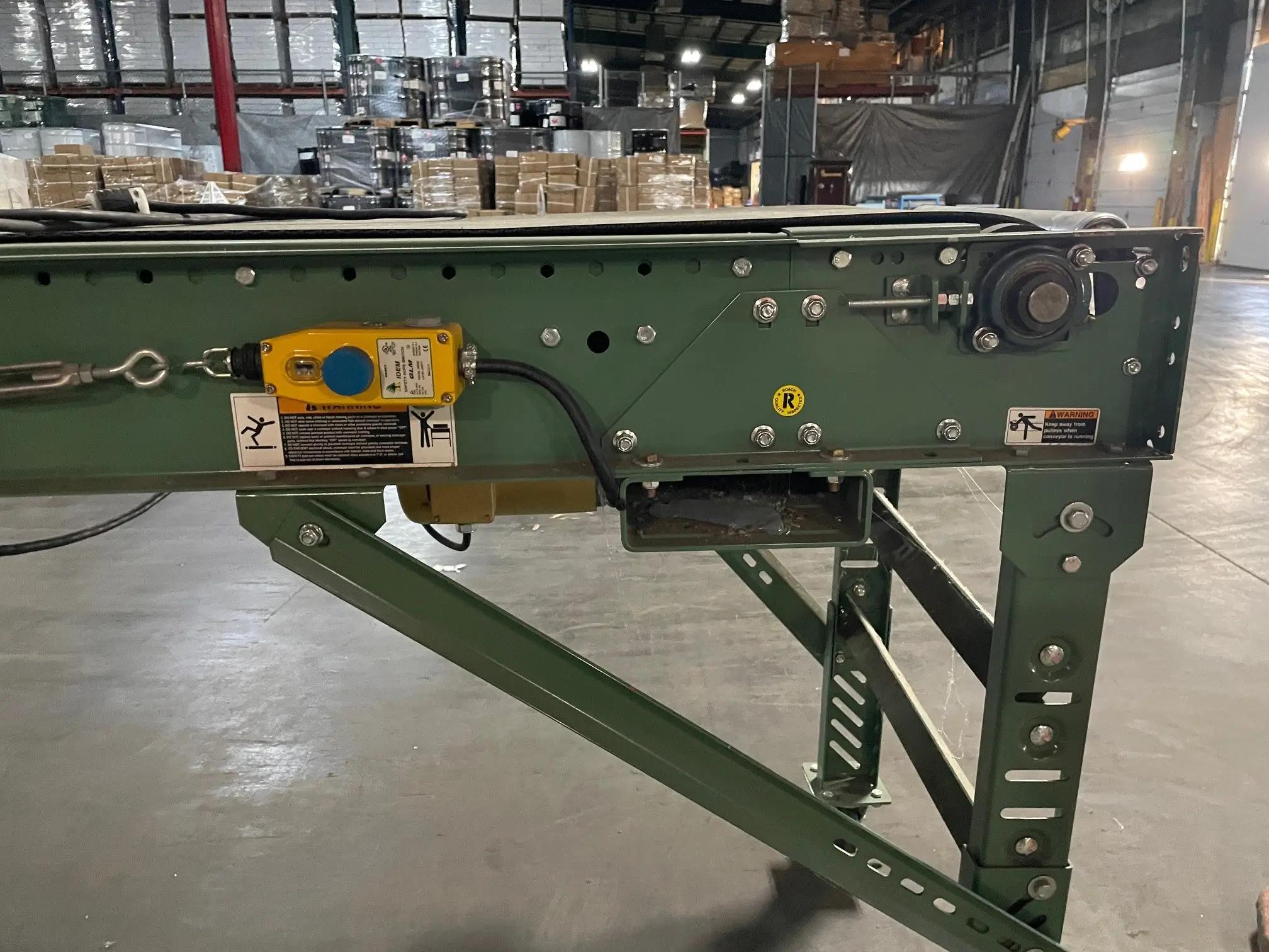 Green industrial conveyor system setup in a warehouse with boxes and pallets in the background.
