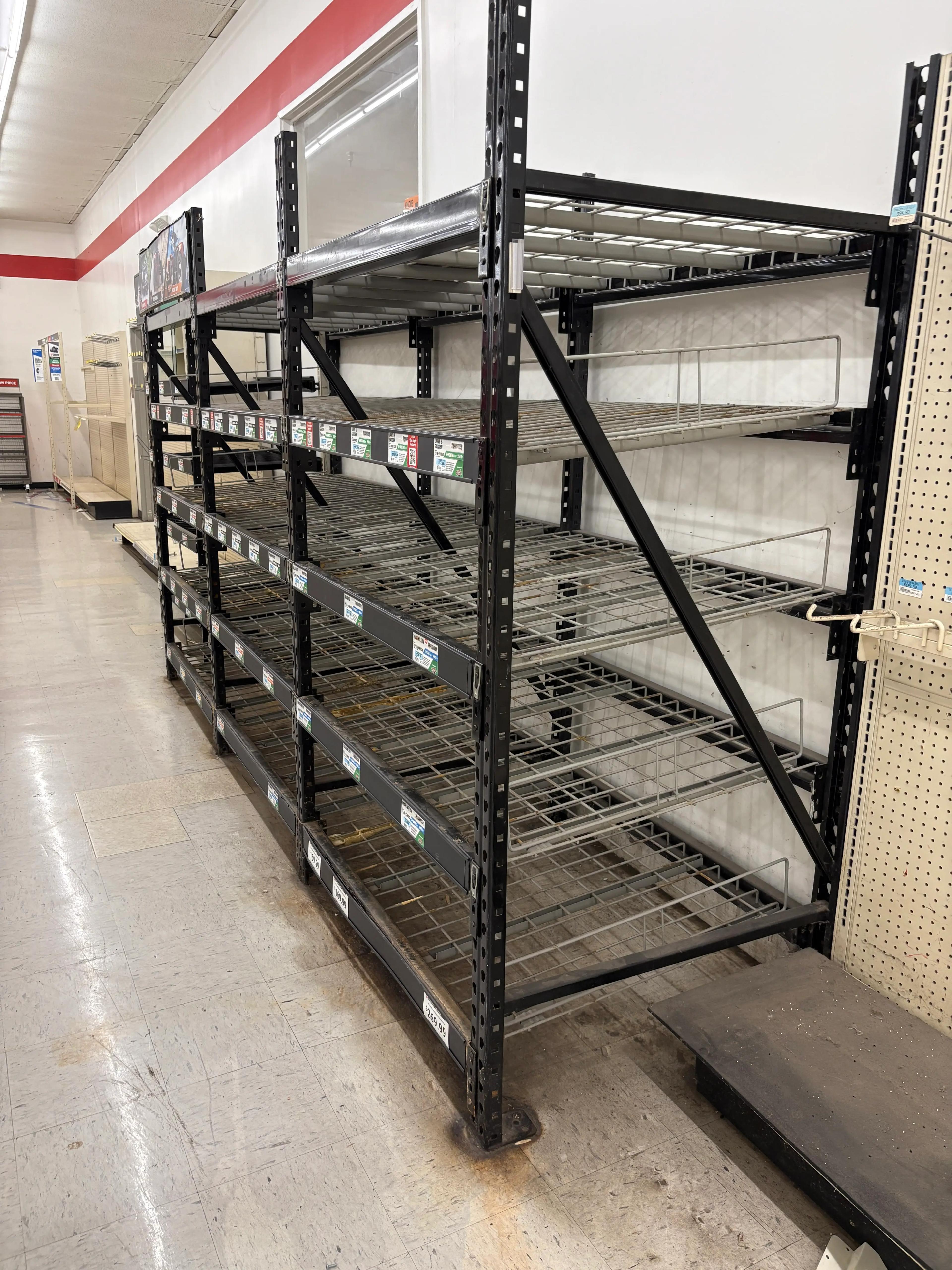 Empty metal shelving units in a store interior with bare floors and a red stripe on the wall.