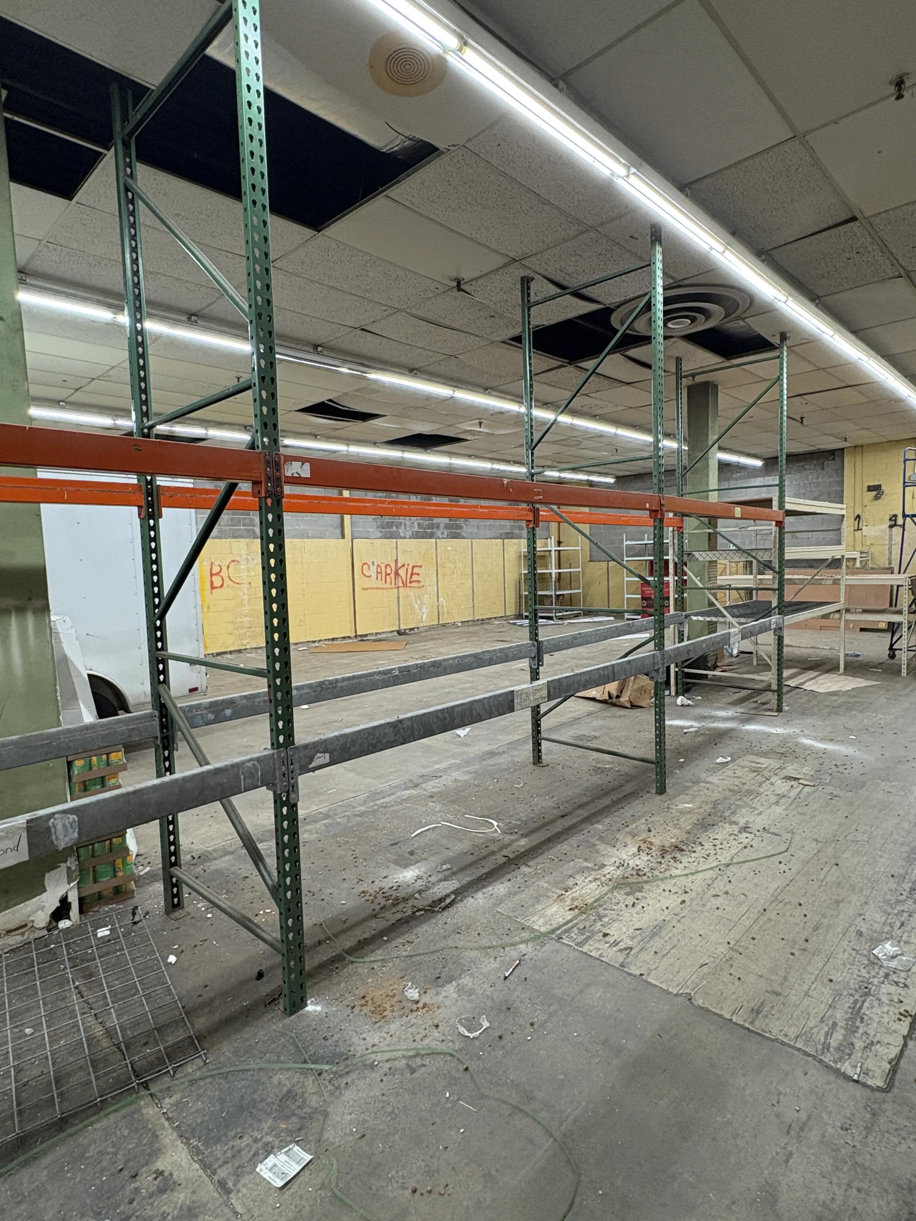 Interior of a warehouse with empty metal shelving units, fluorescent lighting, and a concrete floor.