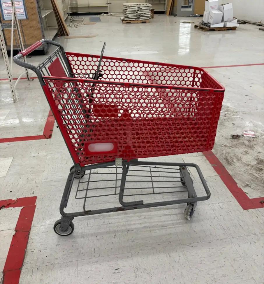 Red shopping cart inside an empty store with linoleum flooring and some construction materials in the background.