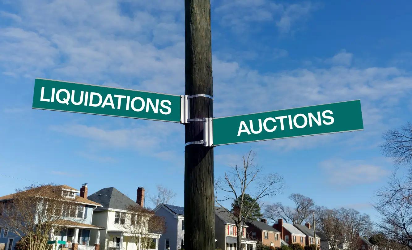 A street sign with directions to Liquidations and Auctions, set against a backdrop of houses and a blue sky.