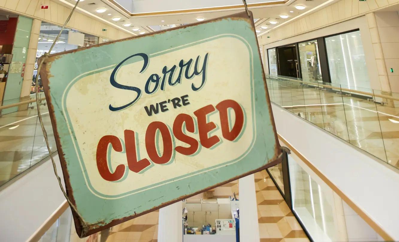 A vintage-style 'Sorry, we're closed' sign hanging in front of a store in a shopping mall.