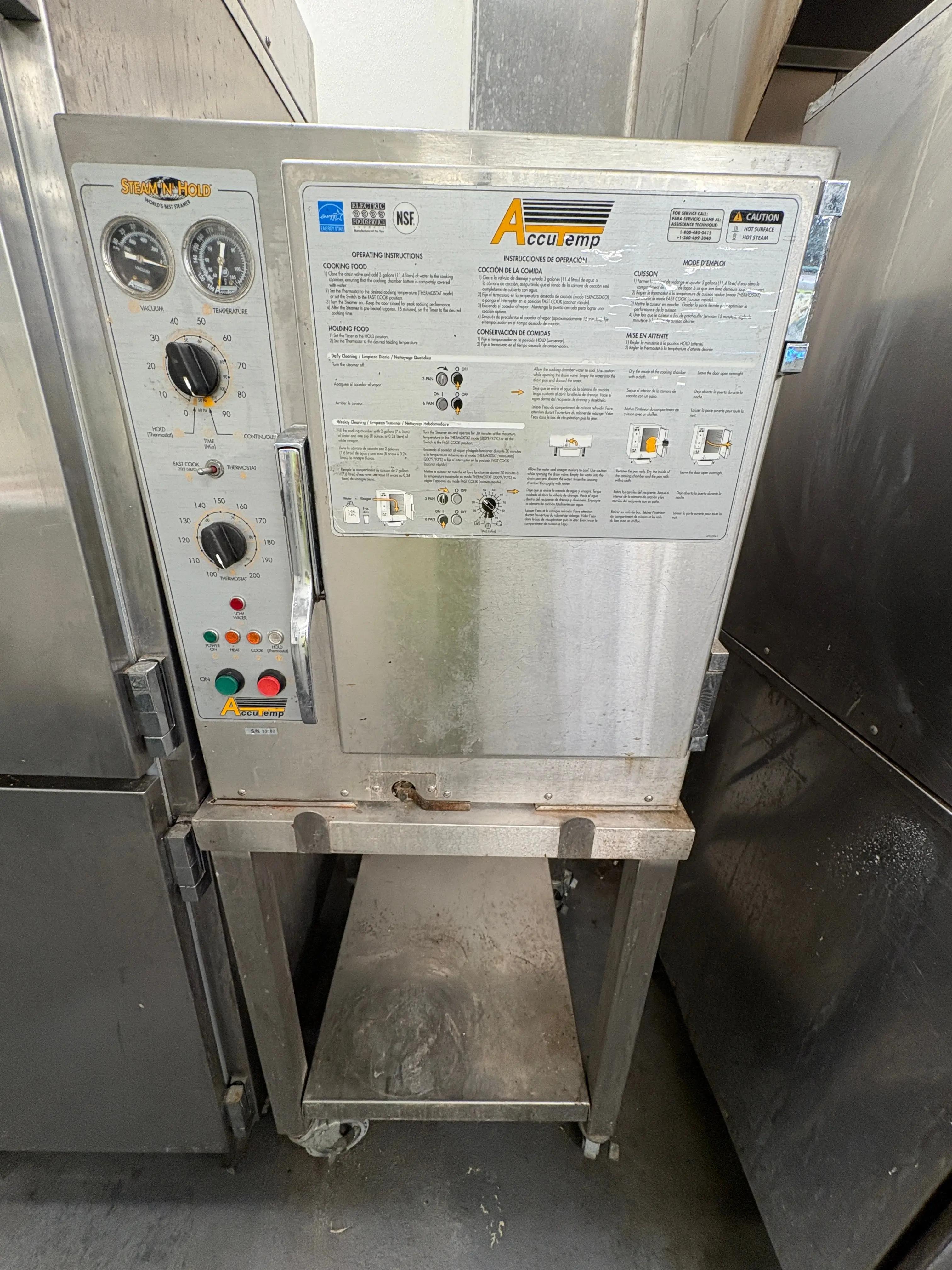 Commercial kitchen steamer labeled "AccuTemp" and "Steam'N'Hold" with a control panel featuring dials and instructions in English, Spanish, and French. The panel includes temperature and timer settings.