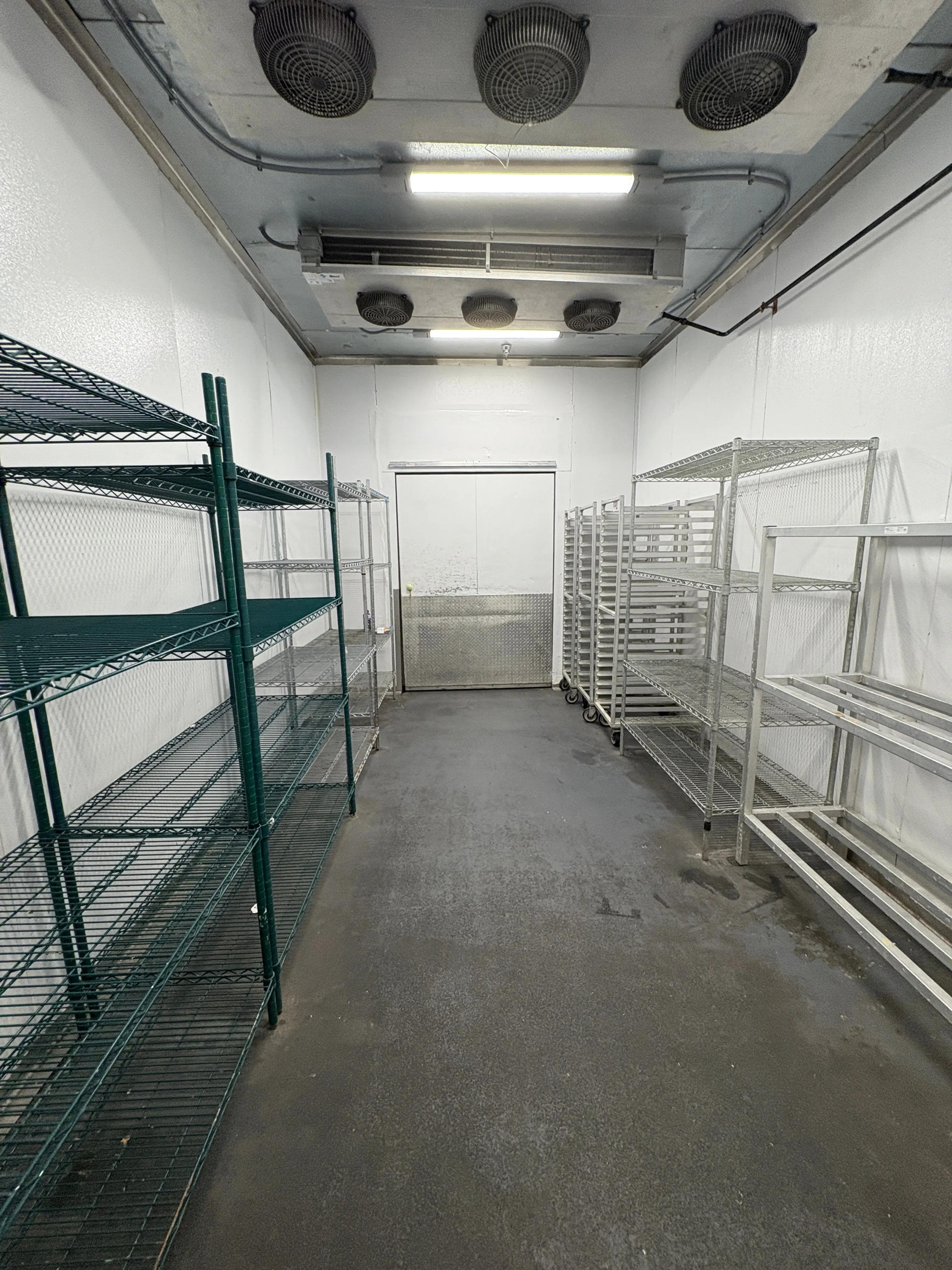 Interior of a commercial cooler room with metal shelves on both sides and ceiling fans.