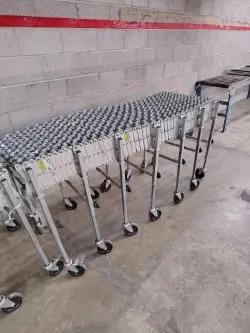 Expandable roller conveyors with metal frames and wheels in an industrial setting, featuring concrete floors and a brick wall.