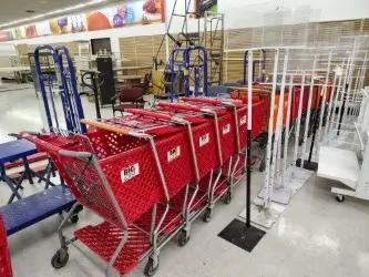 A row of red shopping carts lined up inside a store, with blue dollies and empty display racks visible in the background.