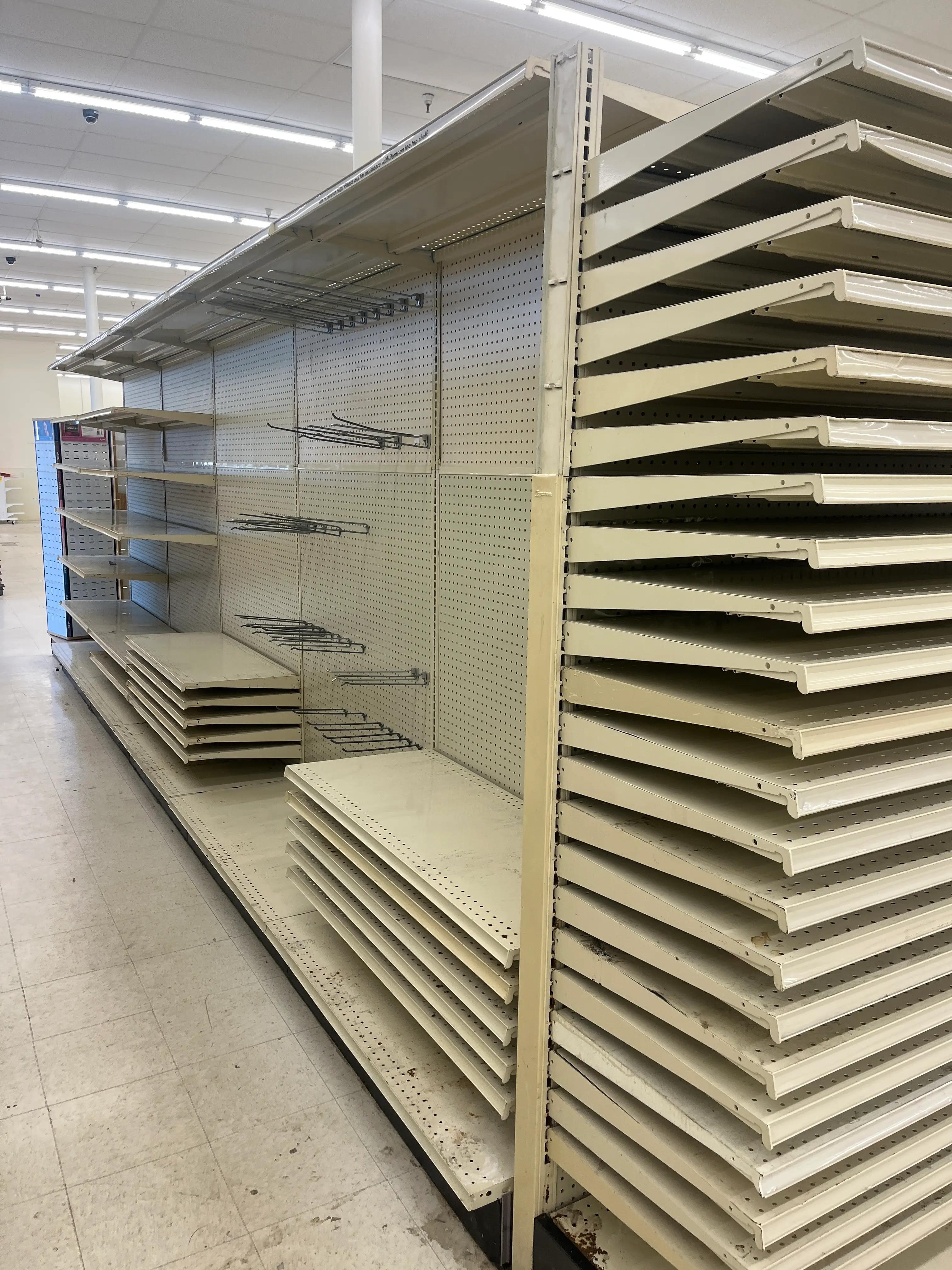 Empty beige retail shelving units and metal shelves are stacked on the floor inside a store with fluorescent lighting and tiled flooring, suggesting a renovation or closure by Mid America.