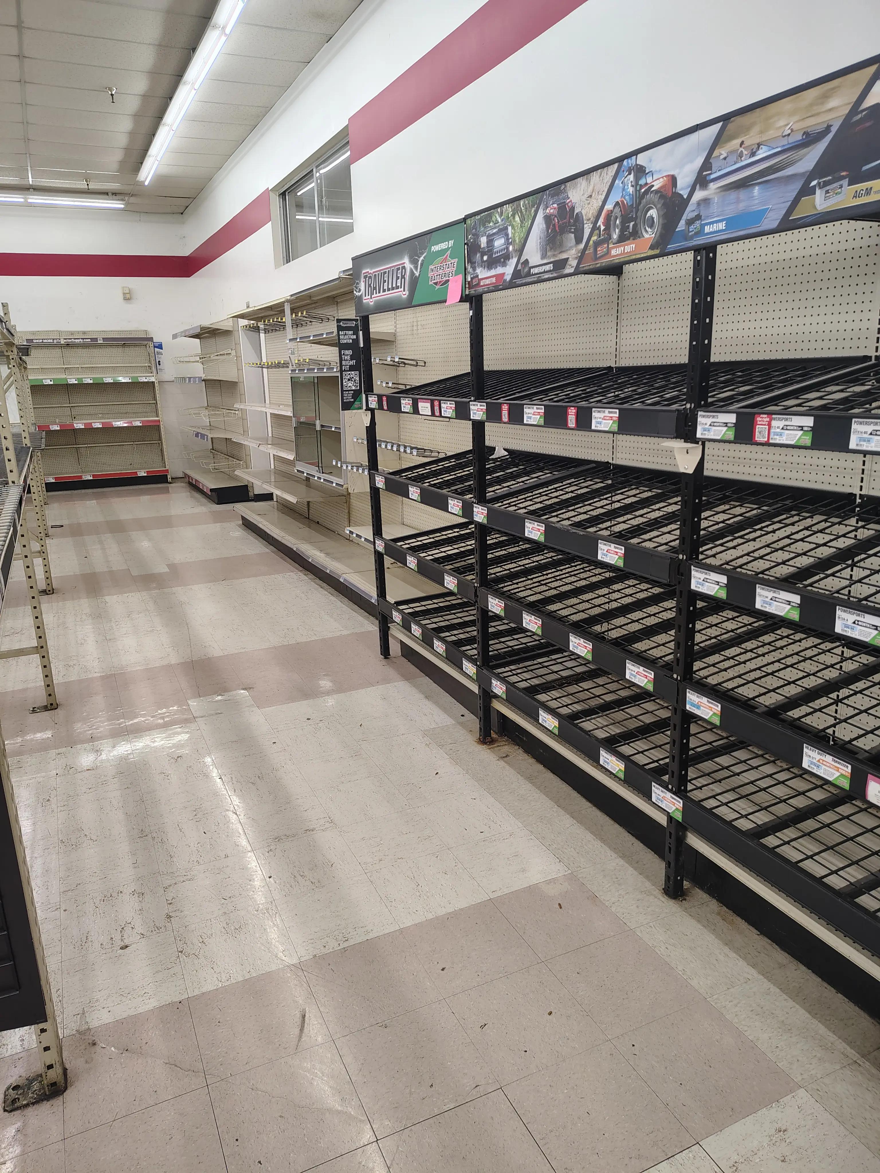 Image of a retail store interior with empty metal shelves and a tiled floor, showing some signage on top.