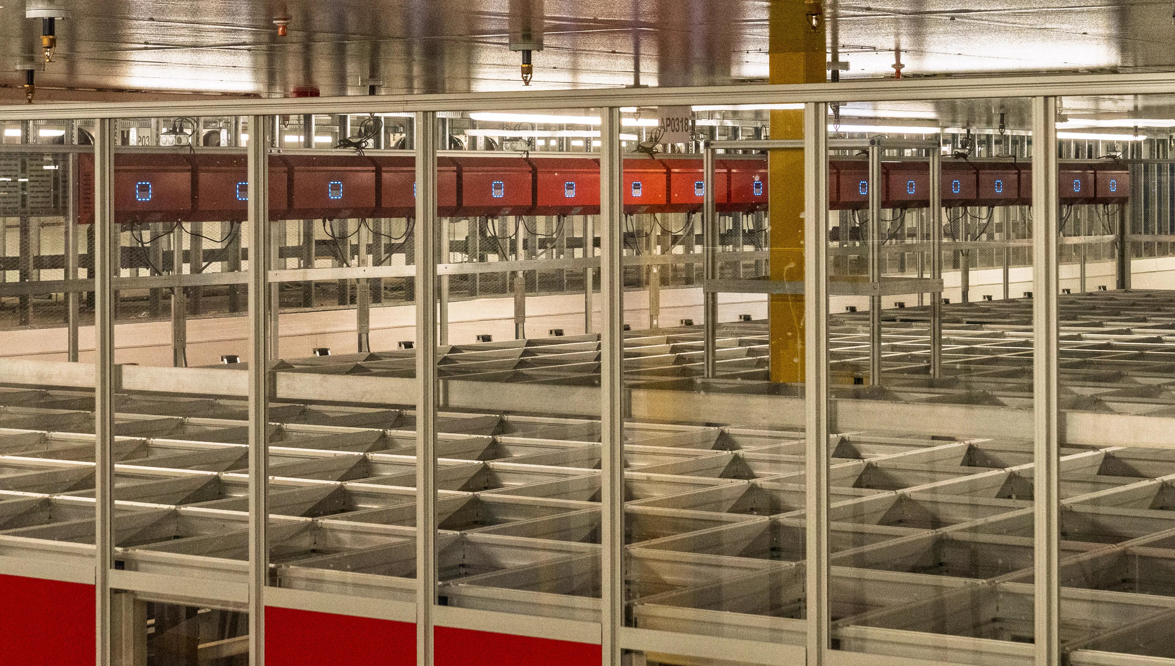 Interior view of an automated storage and retrieval system with red robotic units and metal grid structure in a warehouse setting.