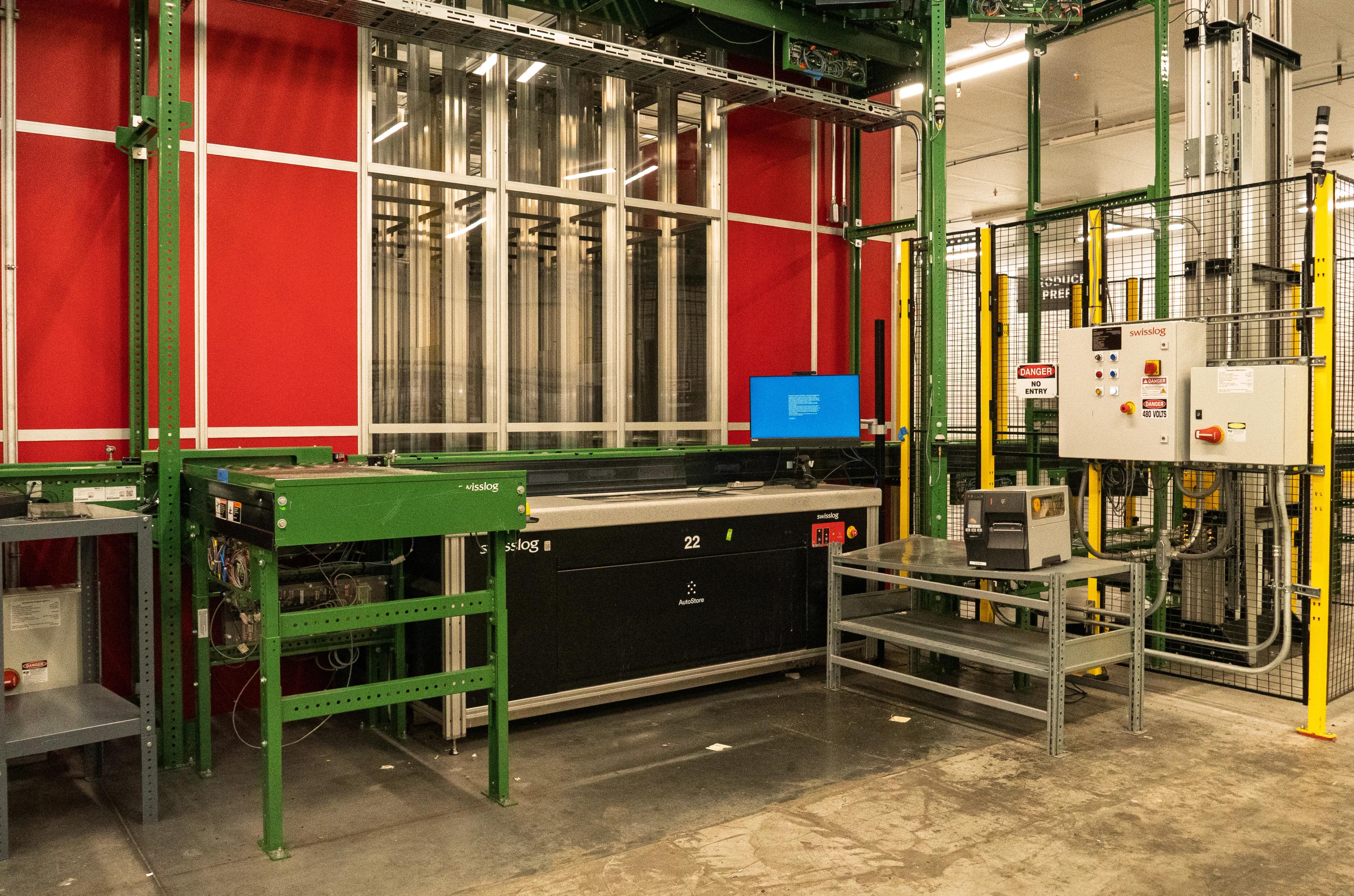 Industrial warehouse environment featuring an automated system with metal structures, a control panel, and safety signage.
