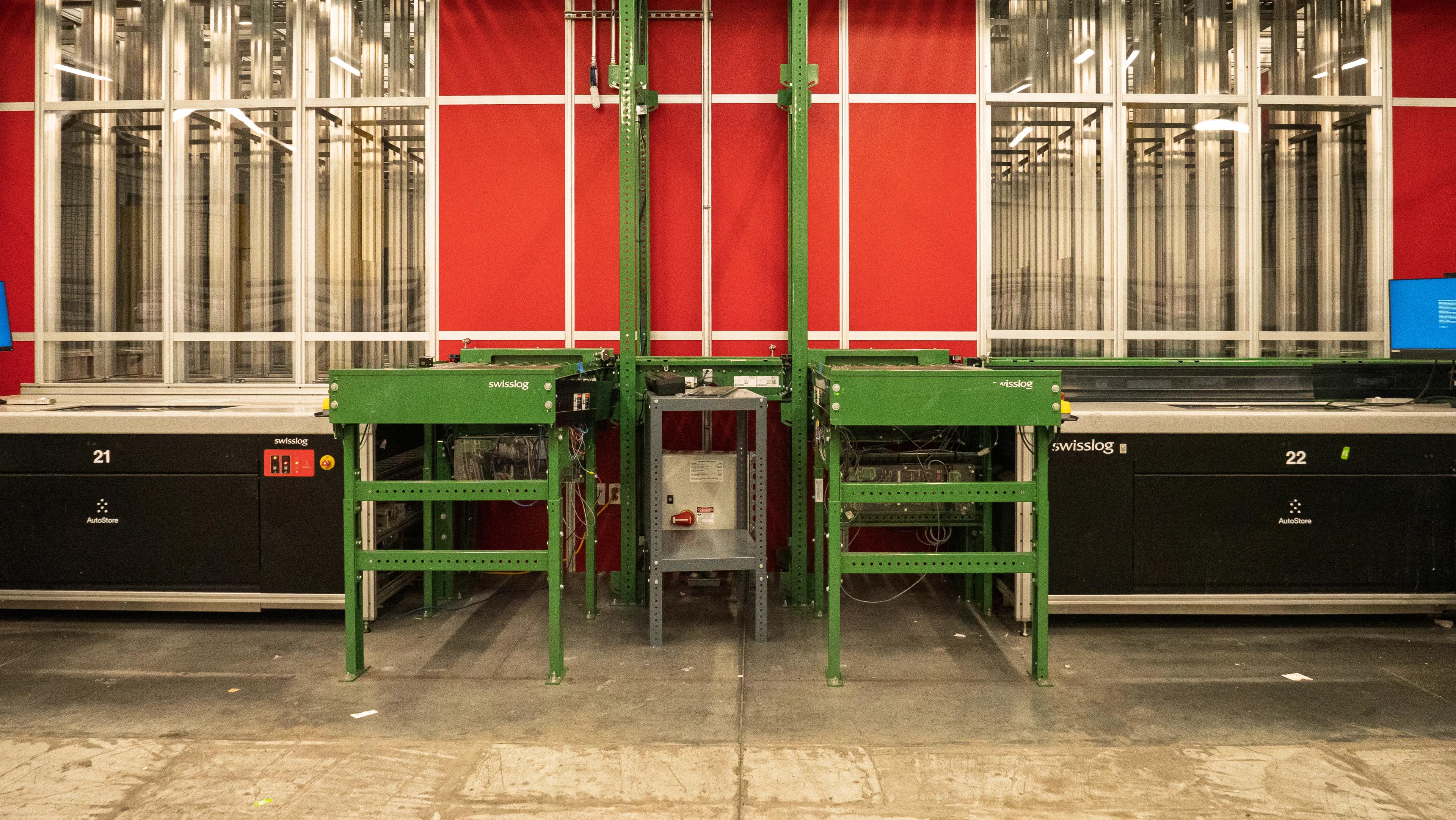 Automated warehouse system with conveyor platform and industrial machinery against a red wall.