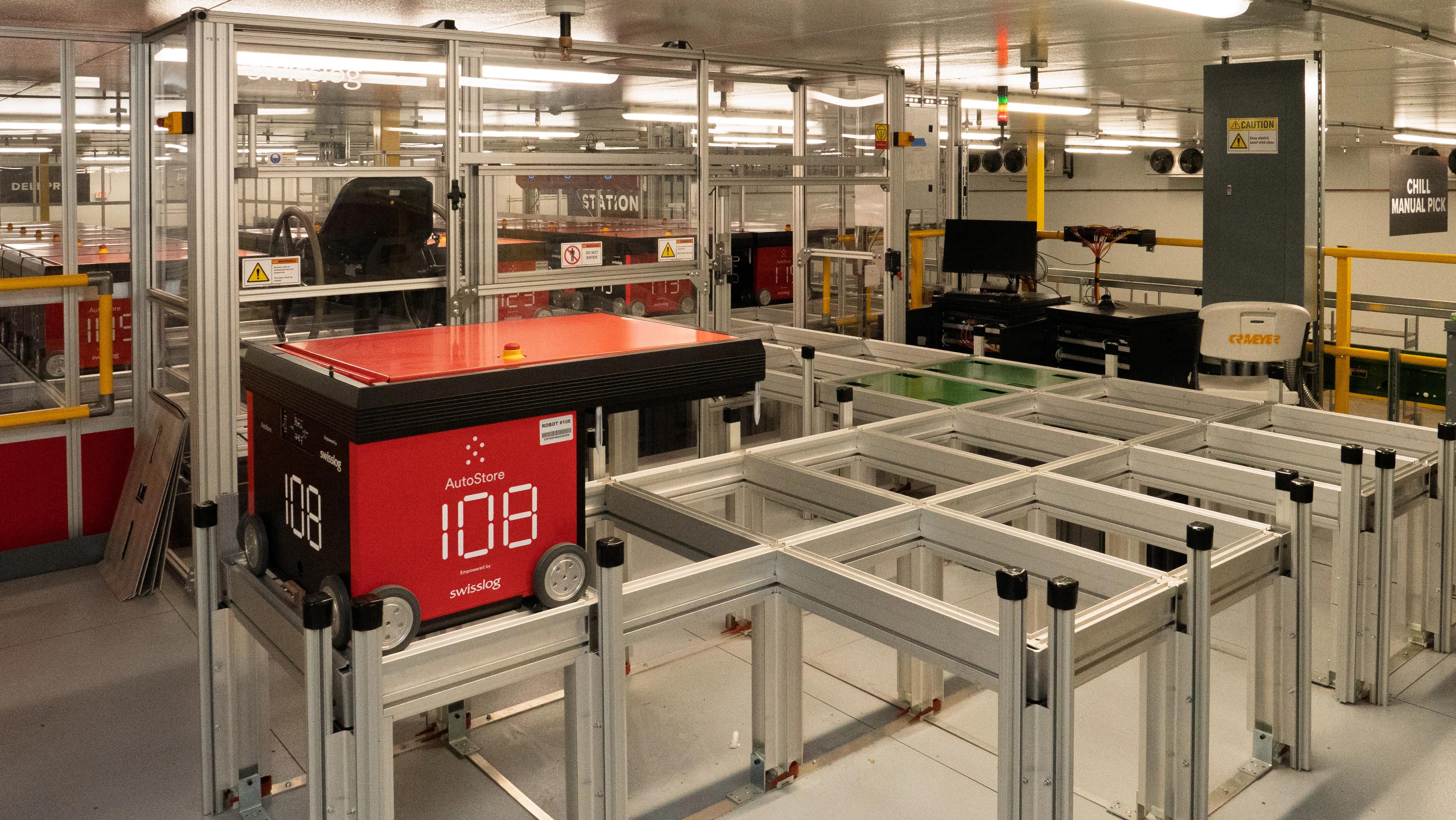 Automated warehouse system with a red AutoStore robotic unit on metal tracks in an industrial setting.