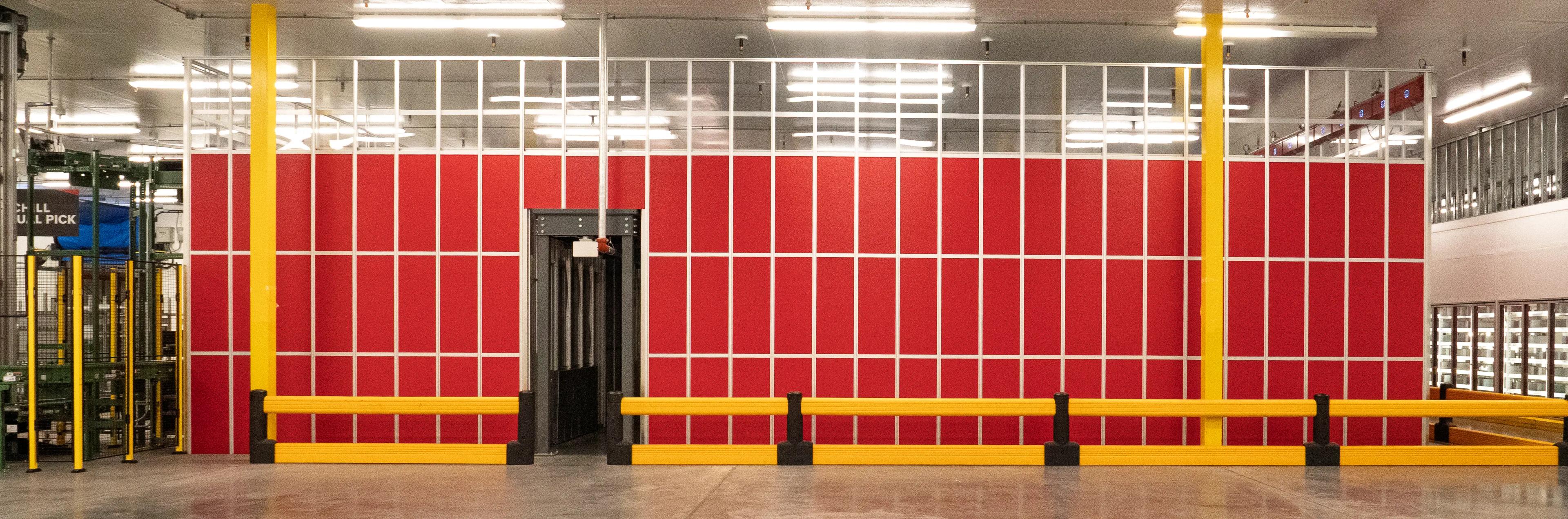 Interior of a warehouse featuring a red wall with structural supports and yellow safety barriers.