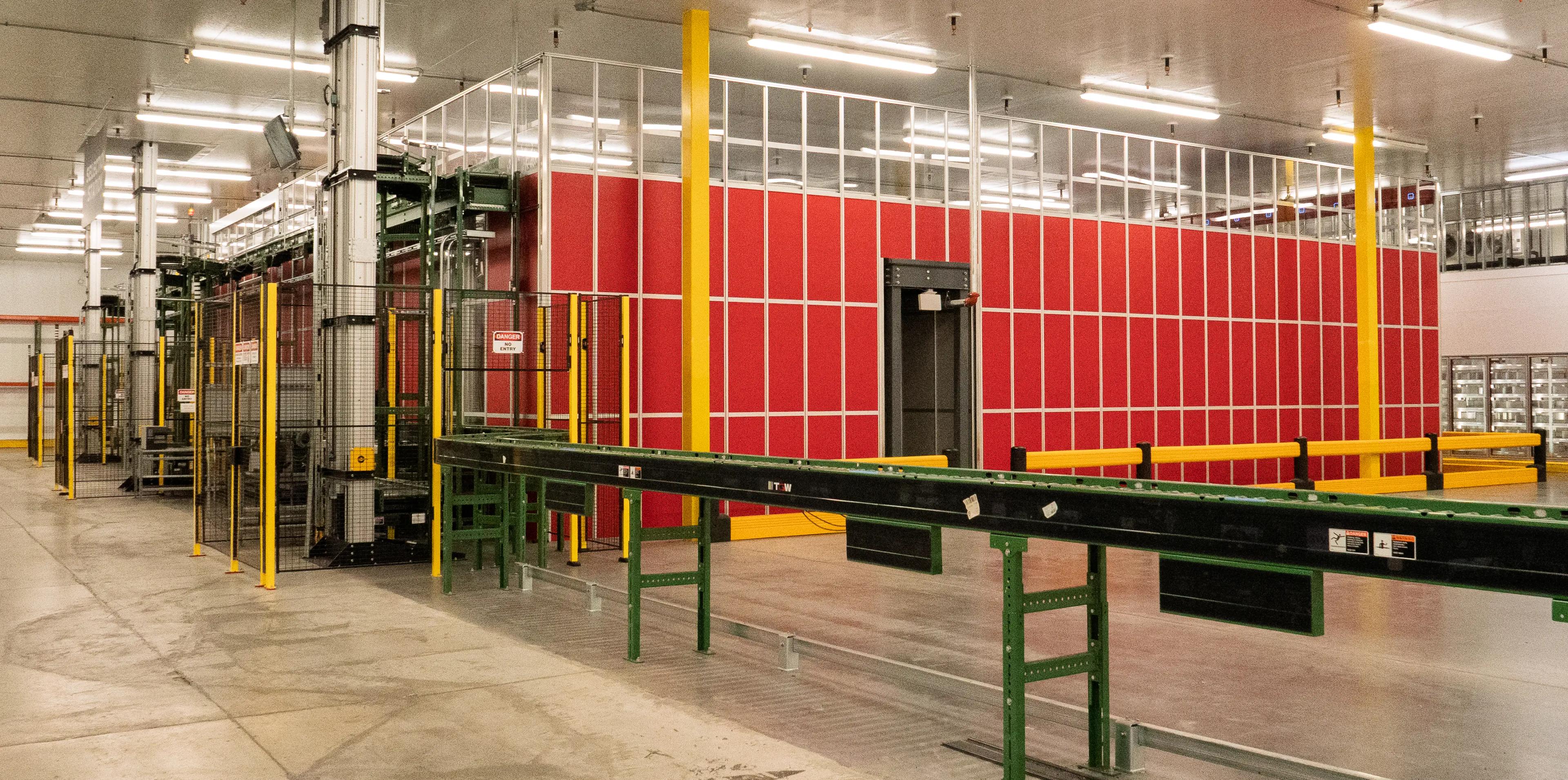 Interior of an industrial facility with conveyor system and red panel walls, featuring safety barriers and machinery.