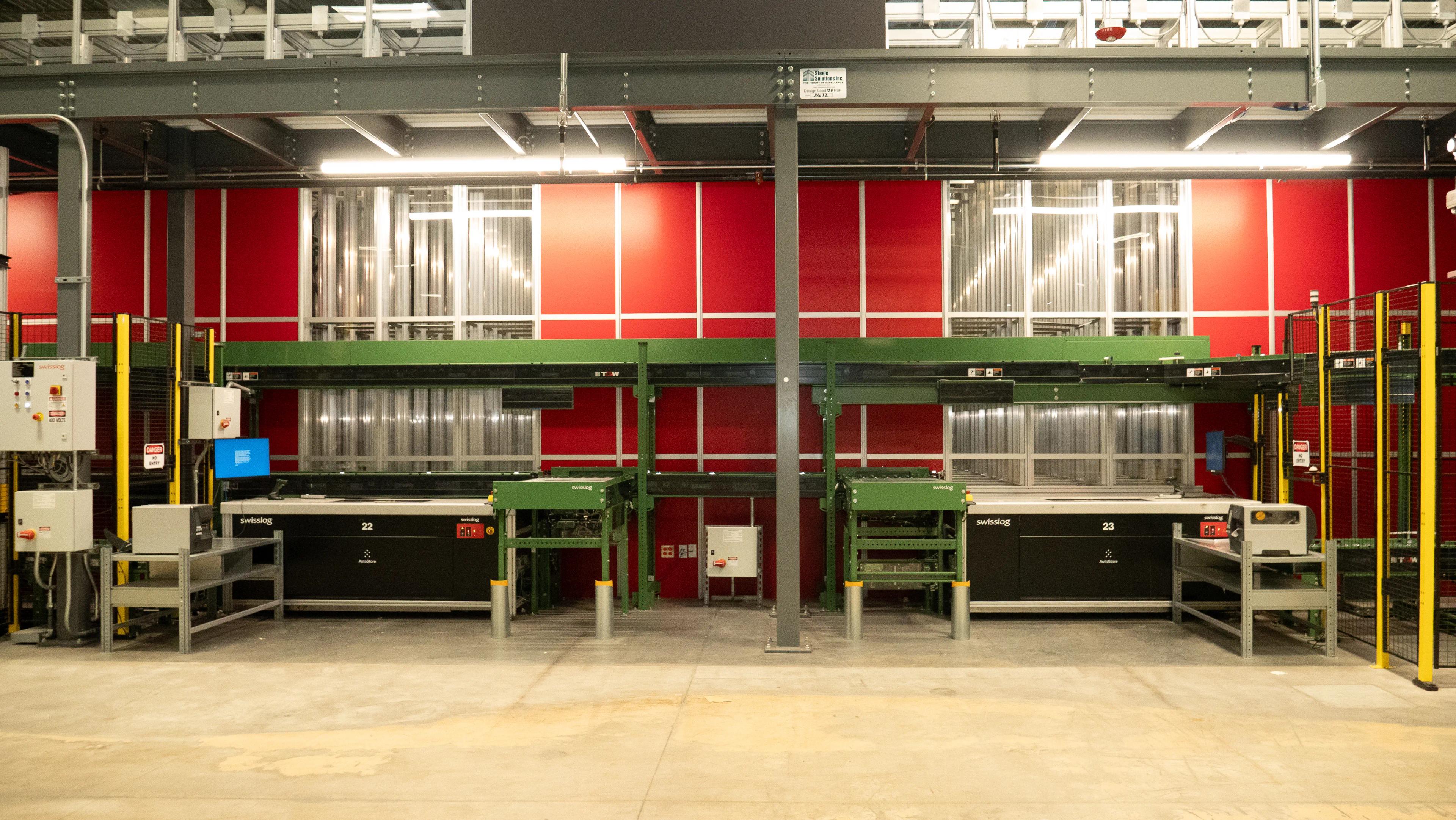 Industrial automated conveyor system with machinery in a warehouse setup, featuring red and green structural elements.