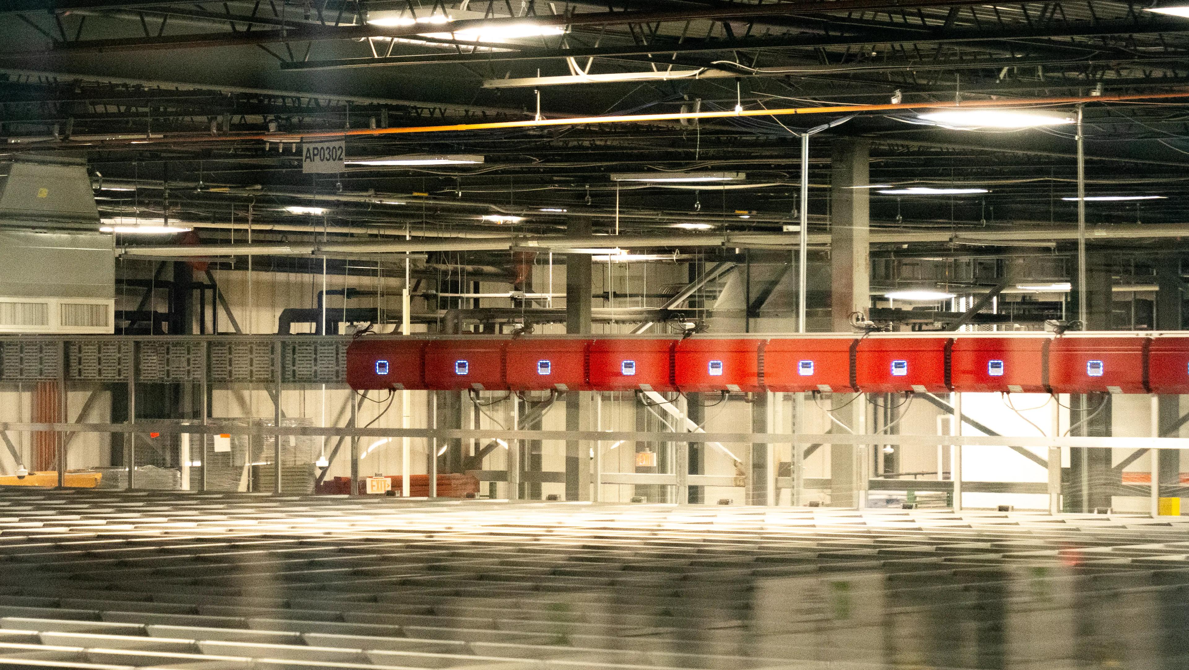 Interior view of a warehouse with overhead lights, automated systems, and a grid of containers.