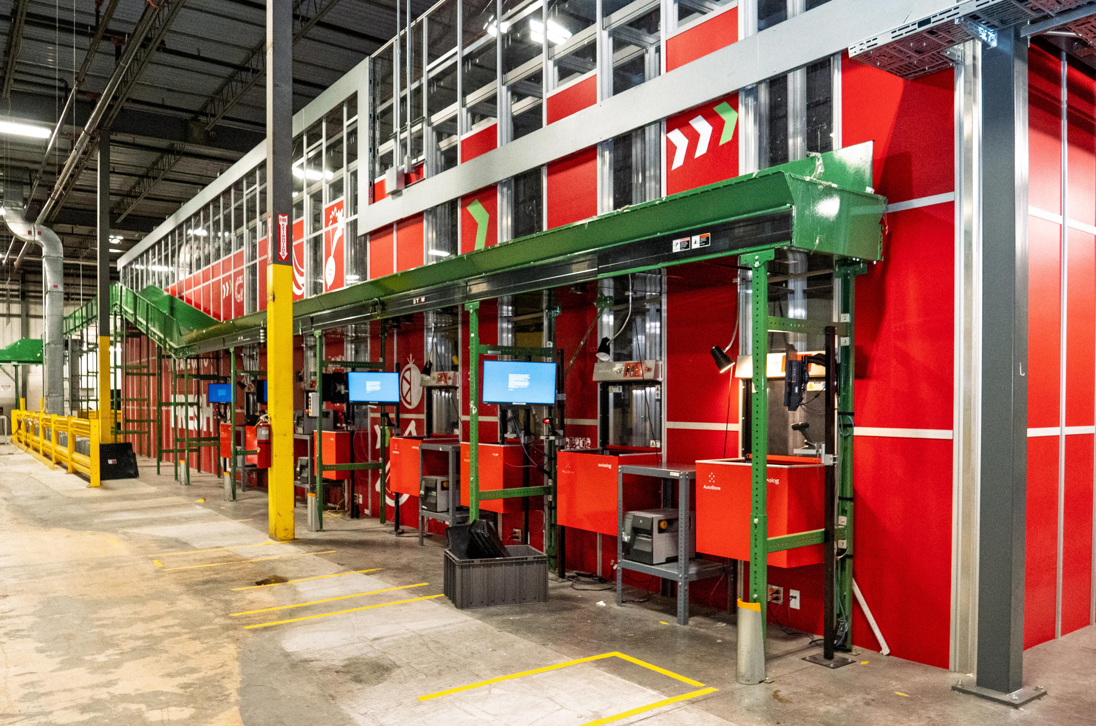Interior of a warehouse featuring red and green industrial machinery with conveyor belts and computer screens.