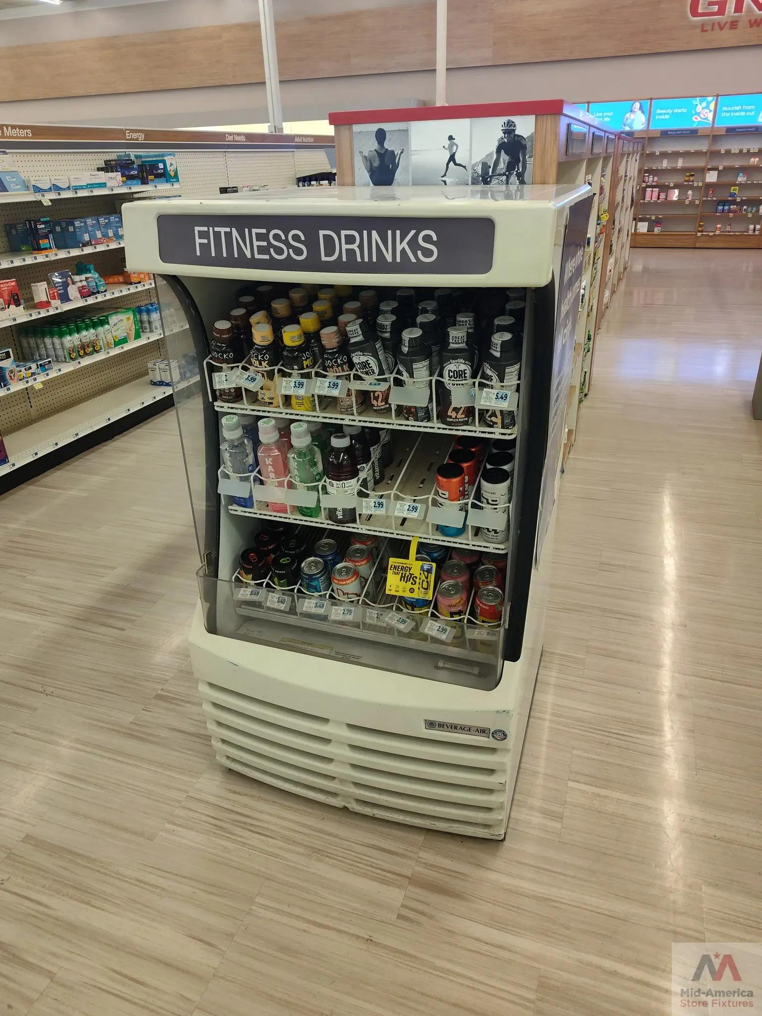 A store display showcasing various fitness drink brands and prices, with a prominent sign labeled "FITNESS DRINKS" and a logo for Mid-America Store Fixtures.