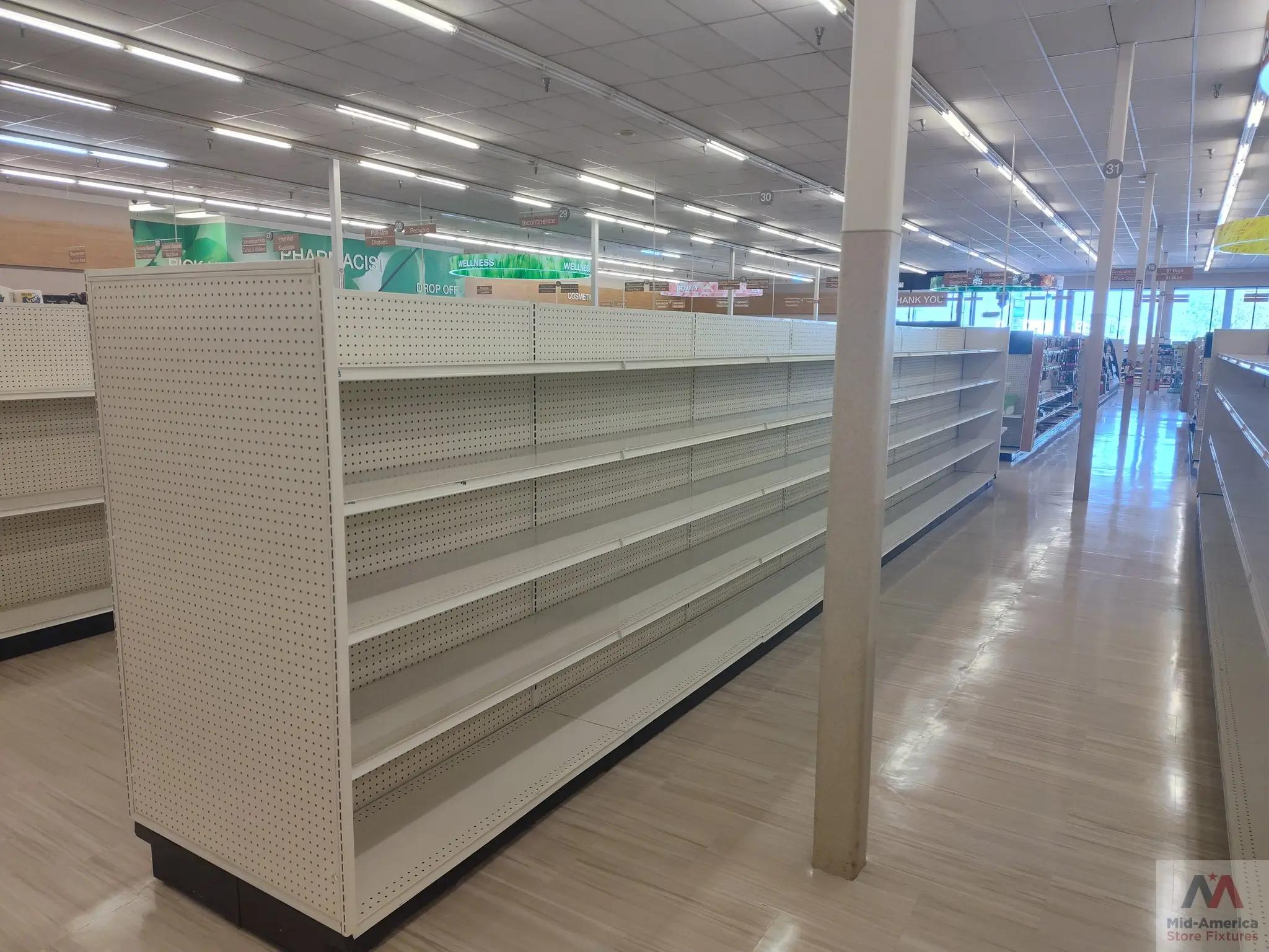 Empty store shelves in a well-lit retail space with pharmacy and wellness signage visible; polished floor; Mid-America Store Fixtures logo in the corner.