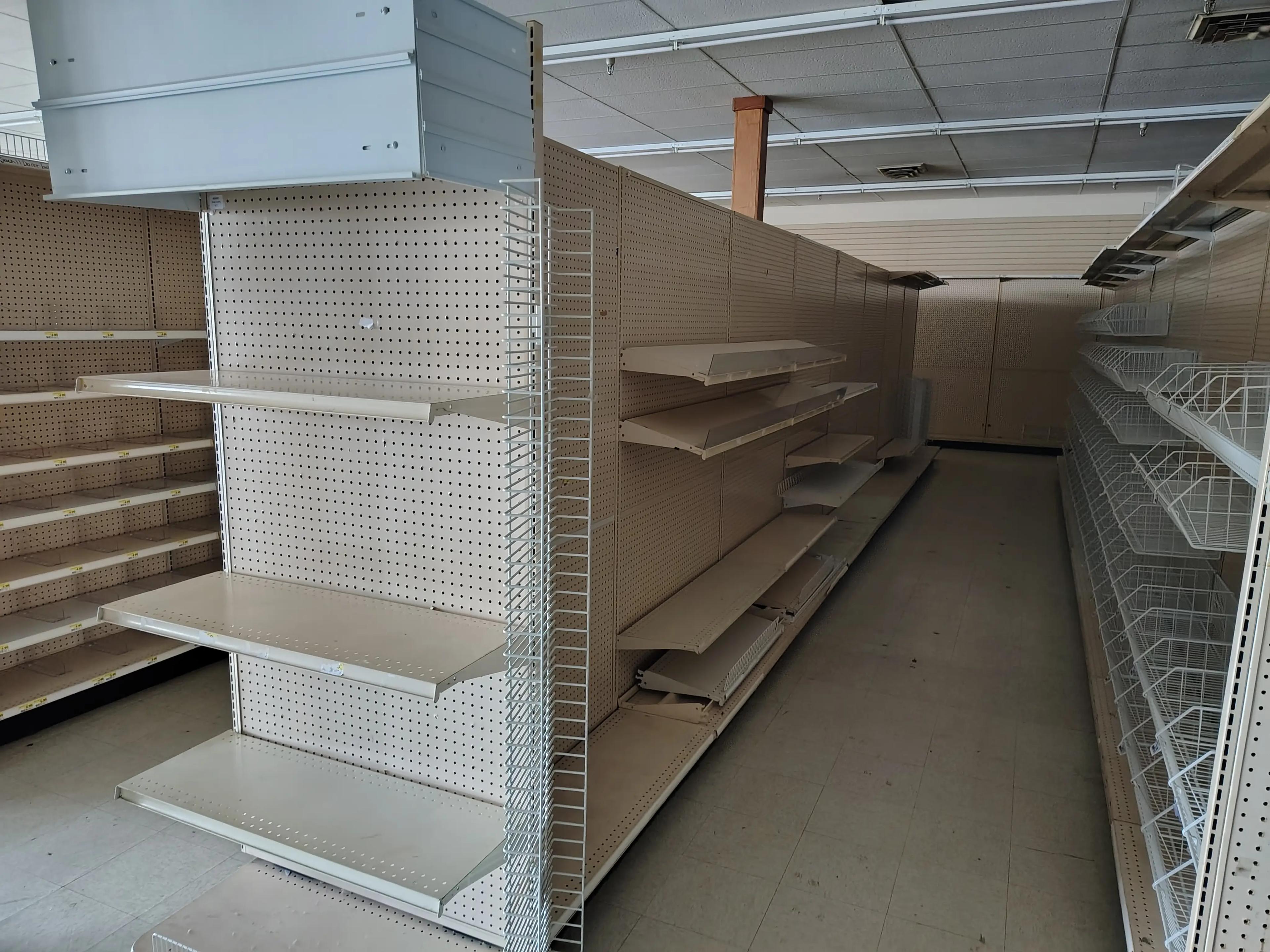 Empty retail store shelves with pegboard backing, metal brackets, and wire baskets, suggesting a store renovation or closure by Mid America.