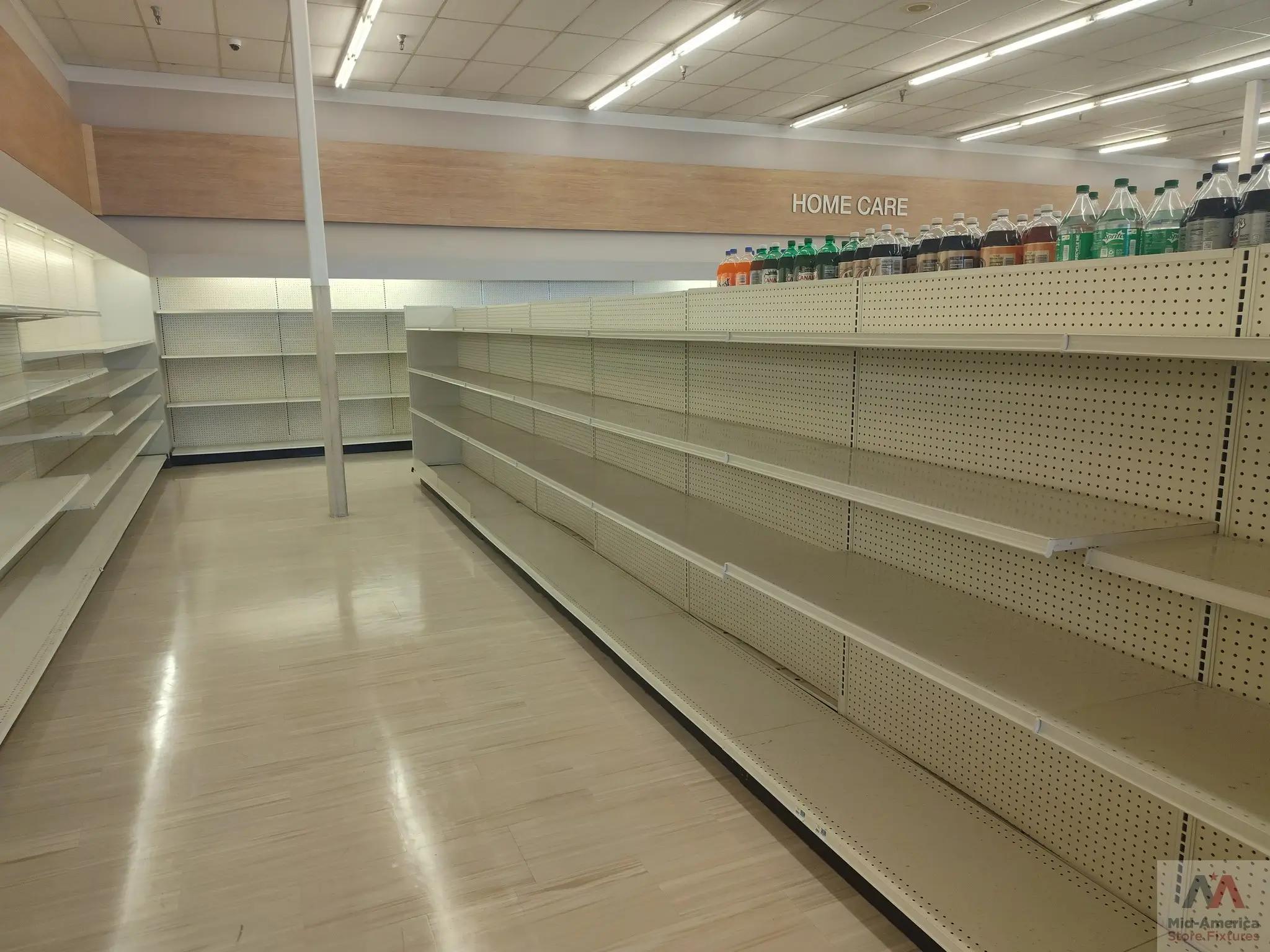 Empty store shelves in a retail space with a "Home Care" sign above. A few bottles are on the top shelf. The floor is light-colored, and the ceiling has fluorescent lighting. Mid-America Store Fixtures logo is visible in the corner.