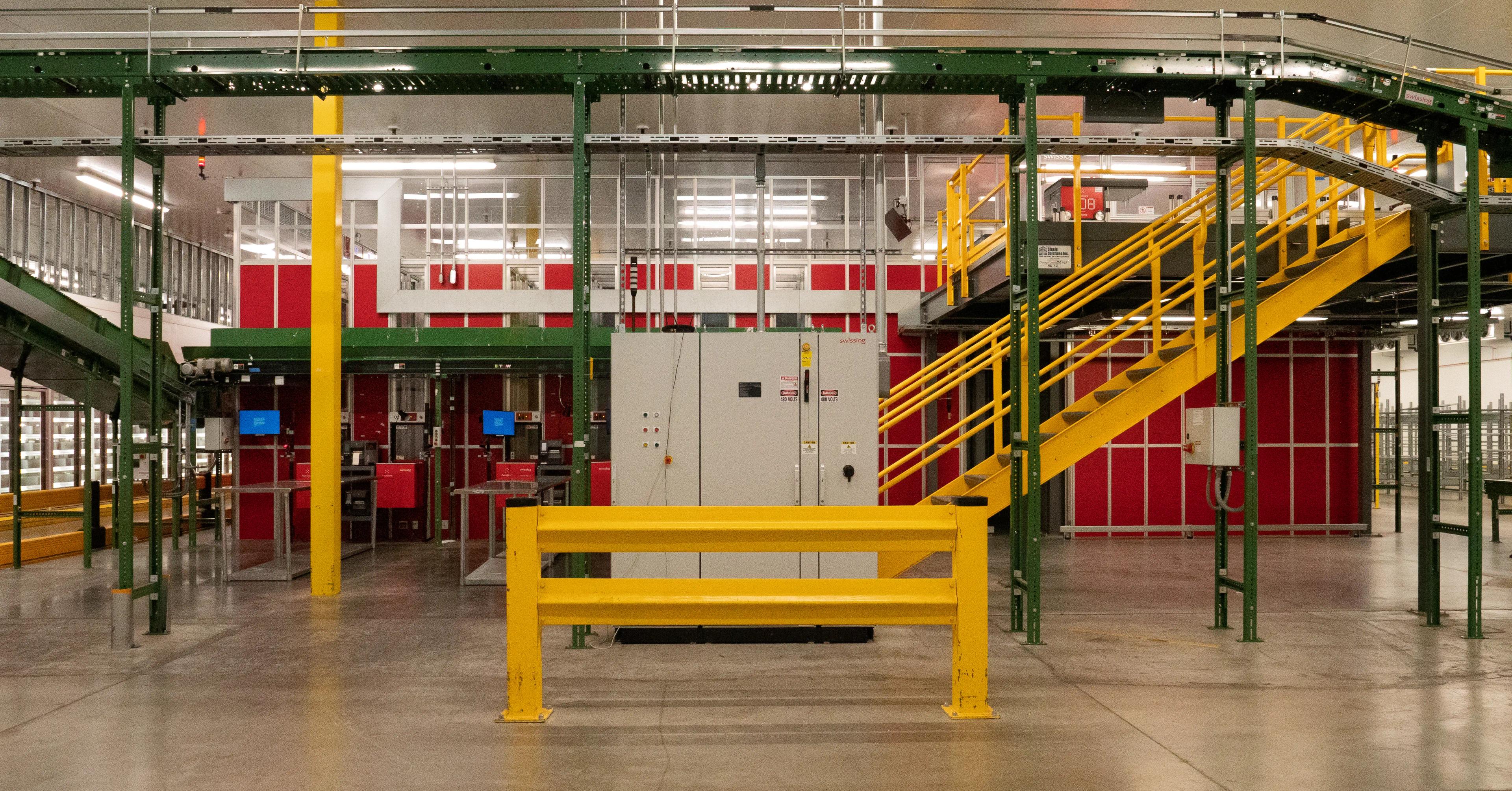 Interior view of an industrial warehouse featuring stairs, equipment, and safety barriers.
