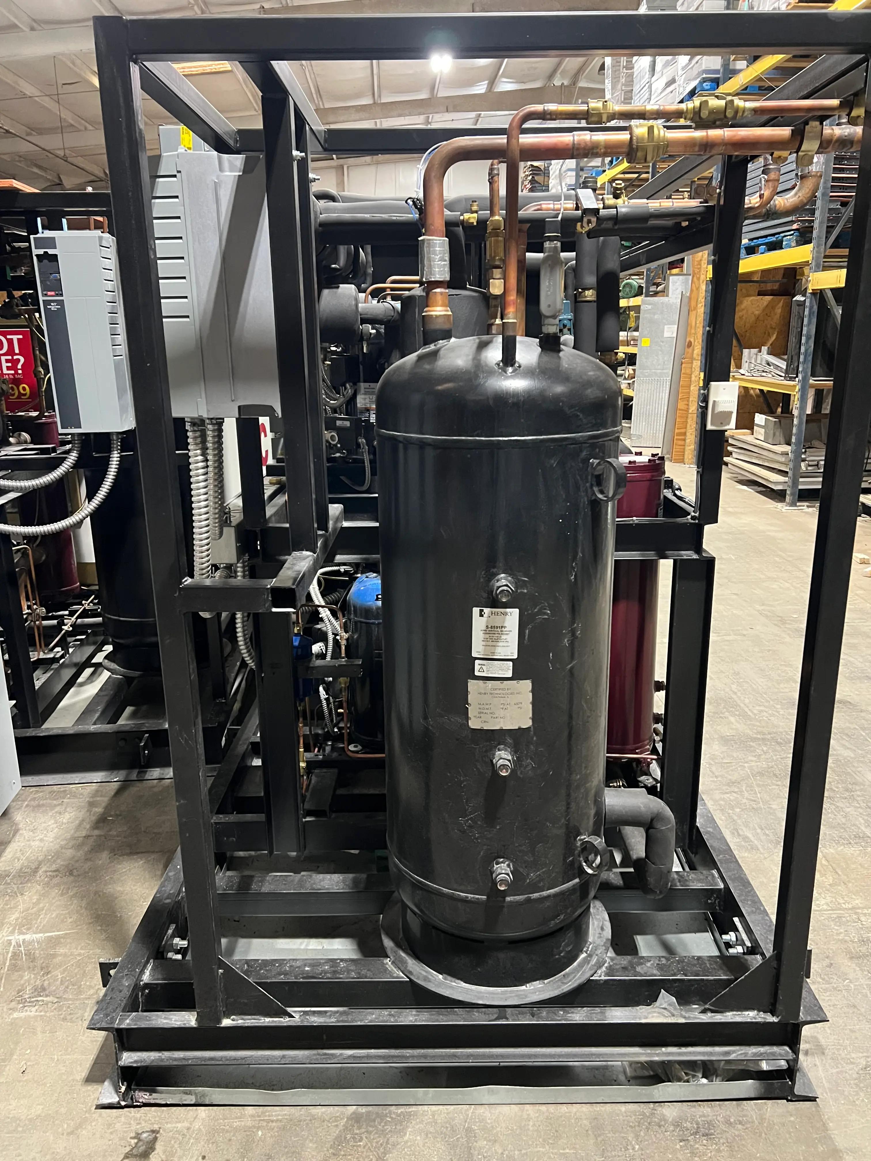 Industrial compressor unit with visible piping and metal framework installed in a facility, surrounded by shelving with various equipment and materials.