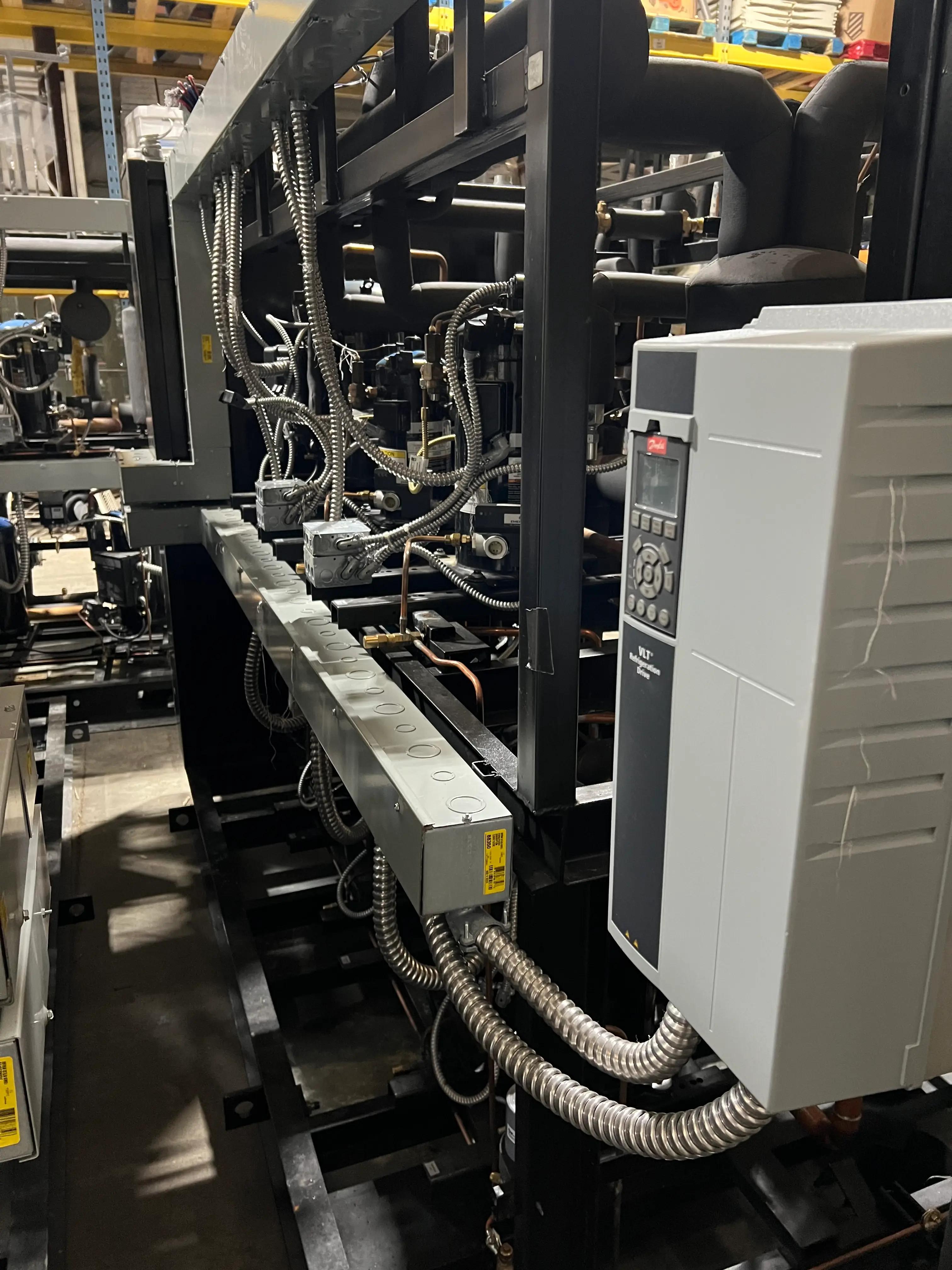 Industrial machinery setup with complex wiring, control panels, and metal pipes in a warehouse setting.