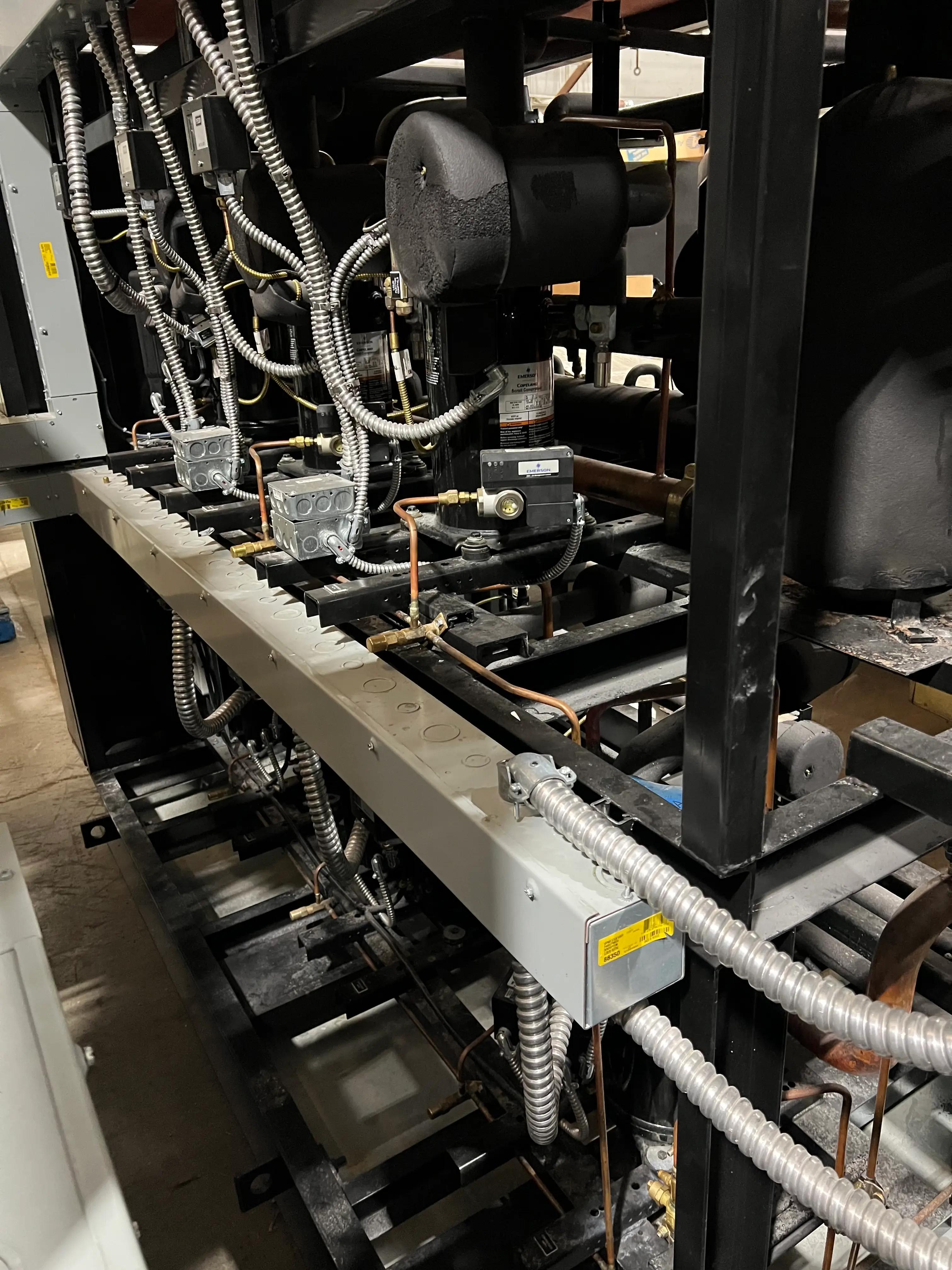 Industrial HVAC system with multiple compressors and metallic piping inside a mechanical room.