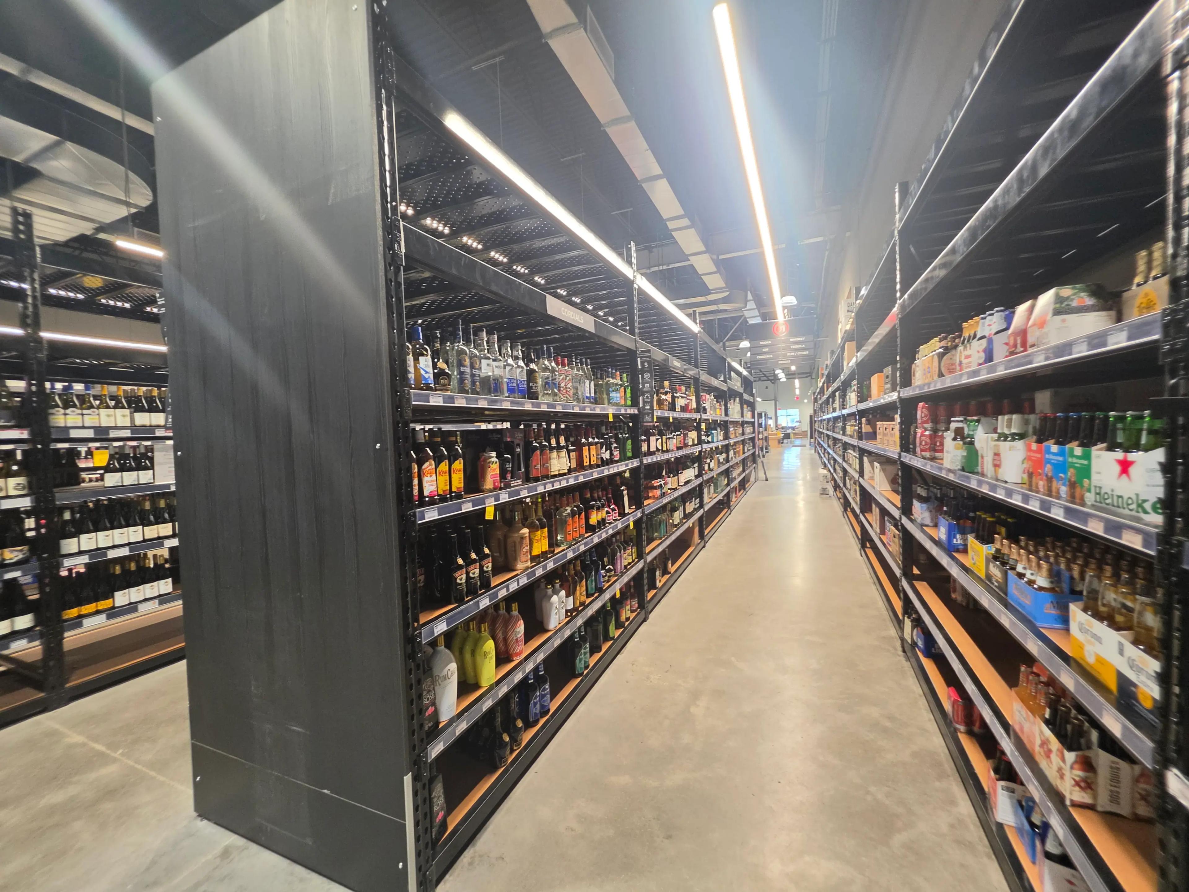 A wide aisle in a liquor store with shelves filled with various bottles and boxes of alcoholic beverages, featuring brands like Heineken and Dos Equis.
