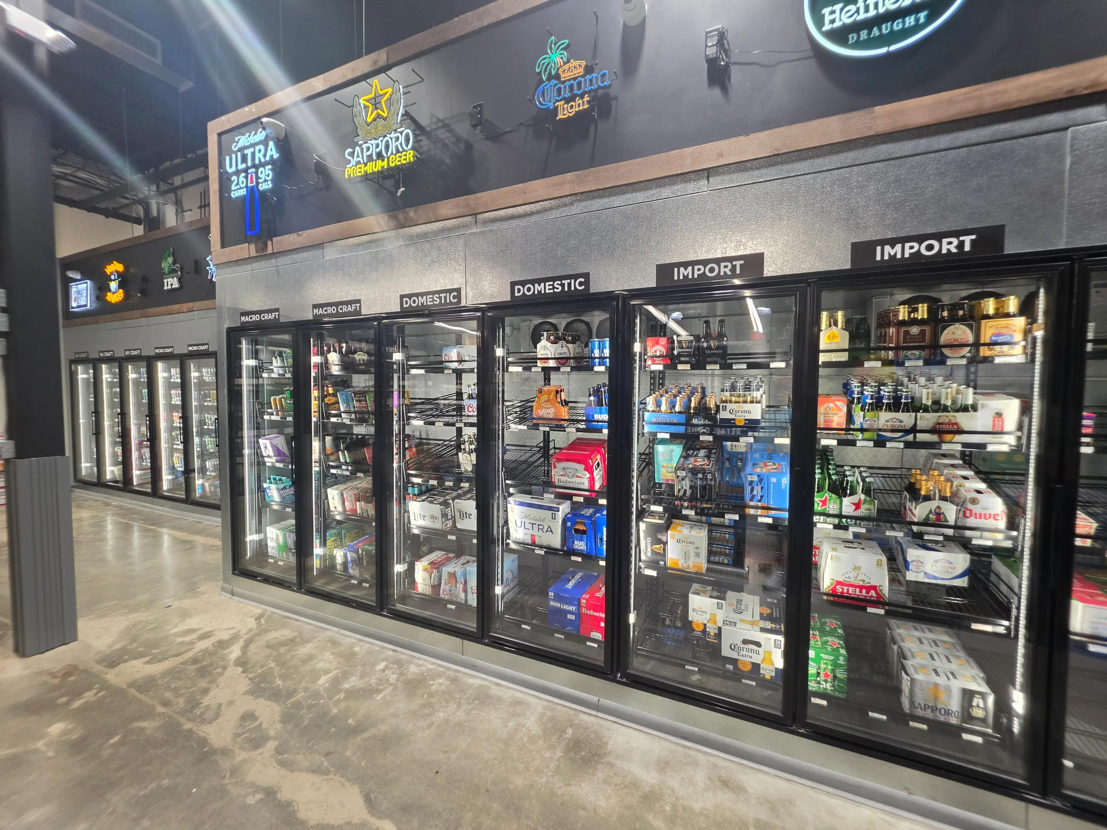 Commercial refrigerator display featuring various beer brands such as Corona, Sapporo, and Stella. Beers are categorized under "Domestic" and "Import" at a Mid America project site.