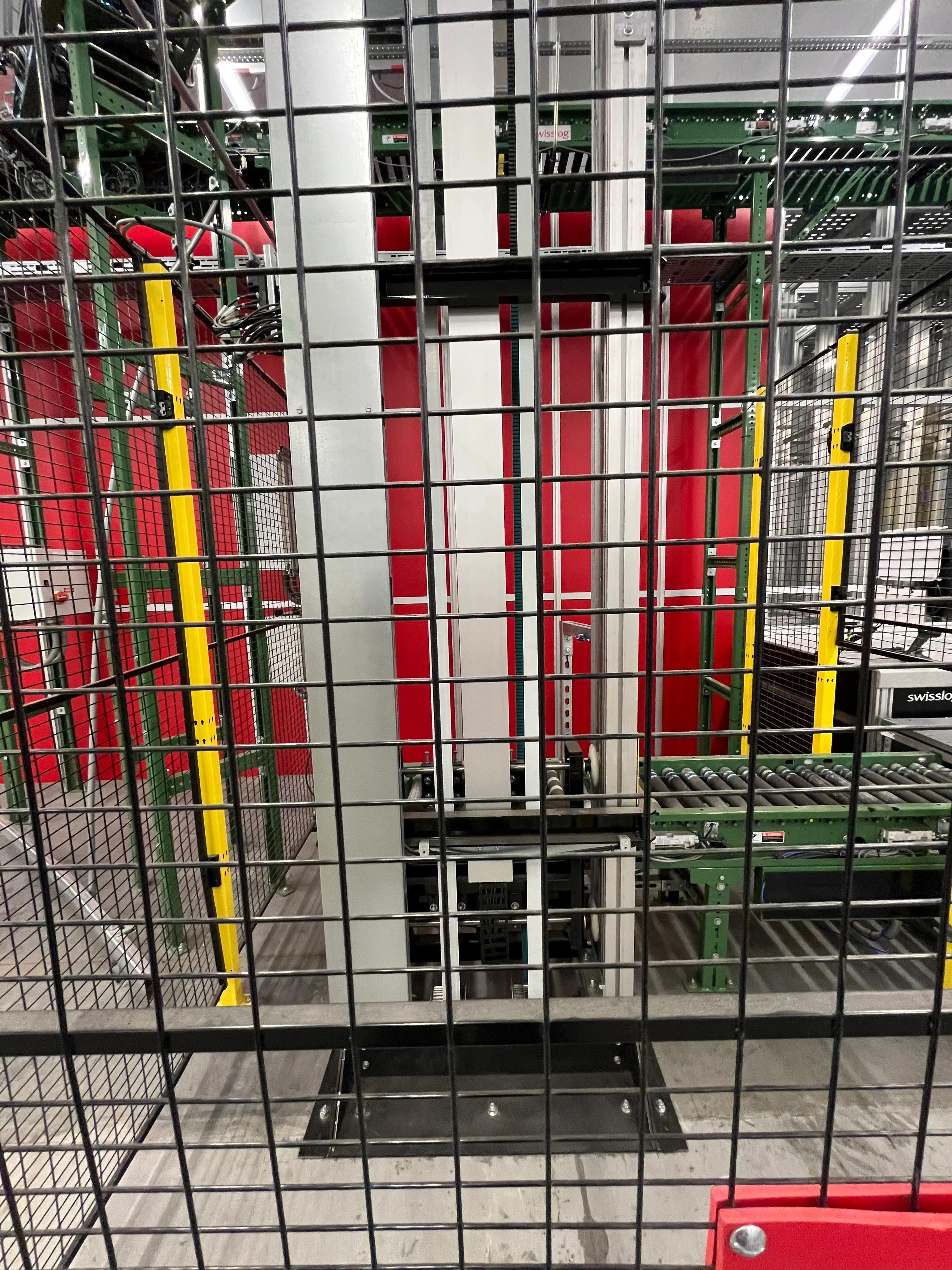 Industrial machinery with metal framework and conveyor belts, enclosed by a safety cage. The setup includes red and yellow structural elements, likely part of a manufacturing or processing facility by Mid America.