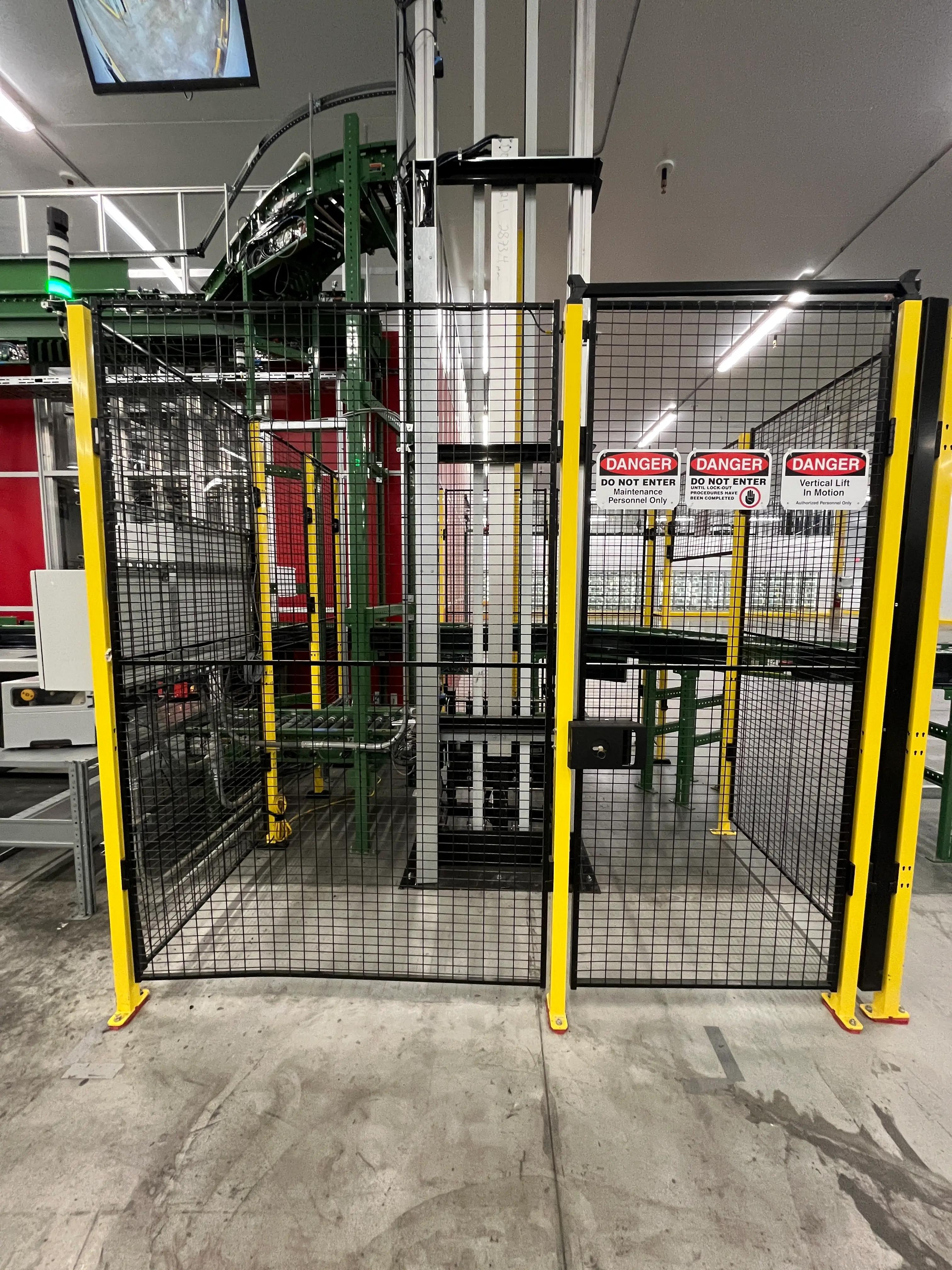 Fenced-off vertical lift area in an industrial setting with machinery and safety barriers. Multiple "Danger" signs warn against entry, indicating maintenance or restricted access.
