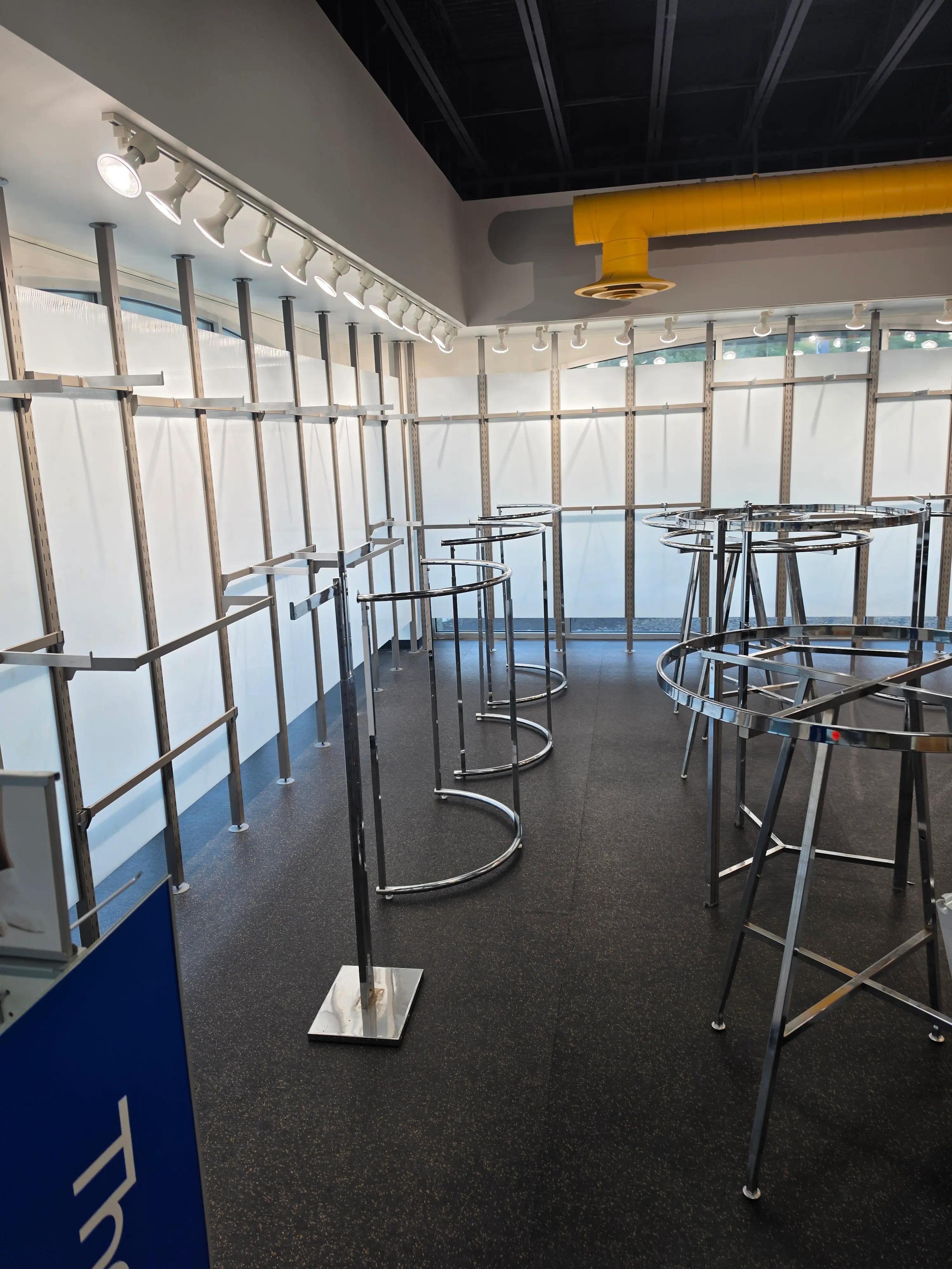 Interior view of a room with a metal framework and track lighting on the ceiling, featuring a prominent yellow ventilation duct and several metal stands on a dark floor.