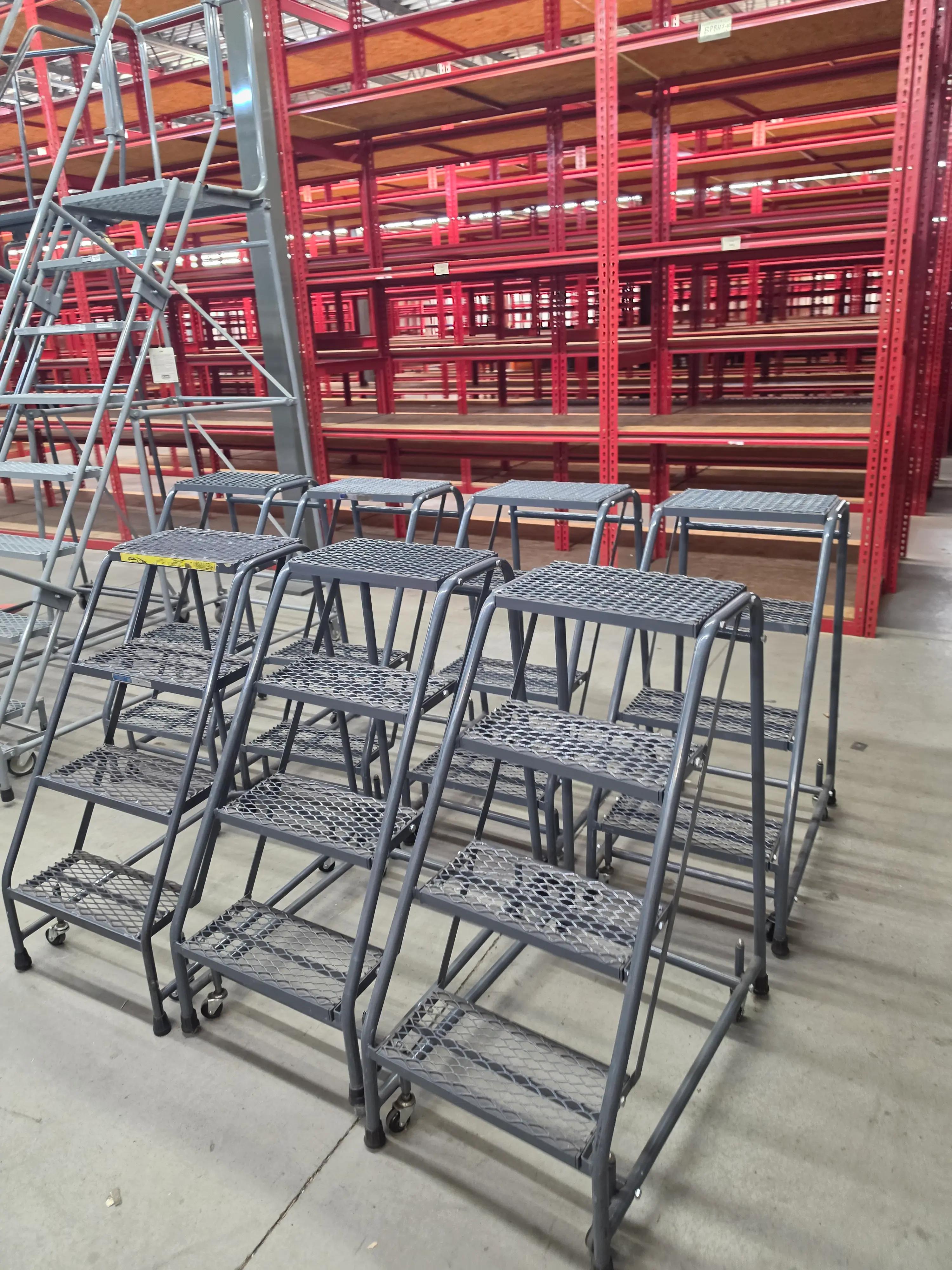 A warehouse with red metal shelving units and several gray rolling ladders on the concrete floor.