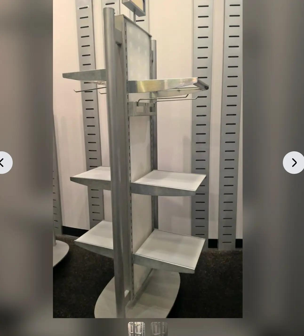 A metal display rack with multiple shelves, designed for retail use, set against a wall with vertical slotted panels.