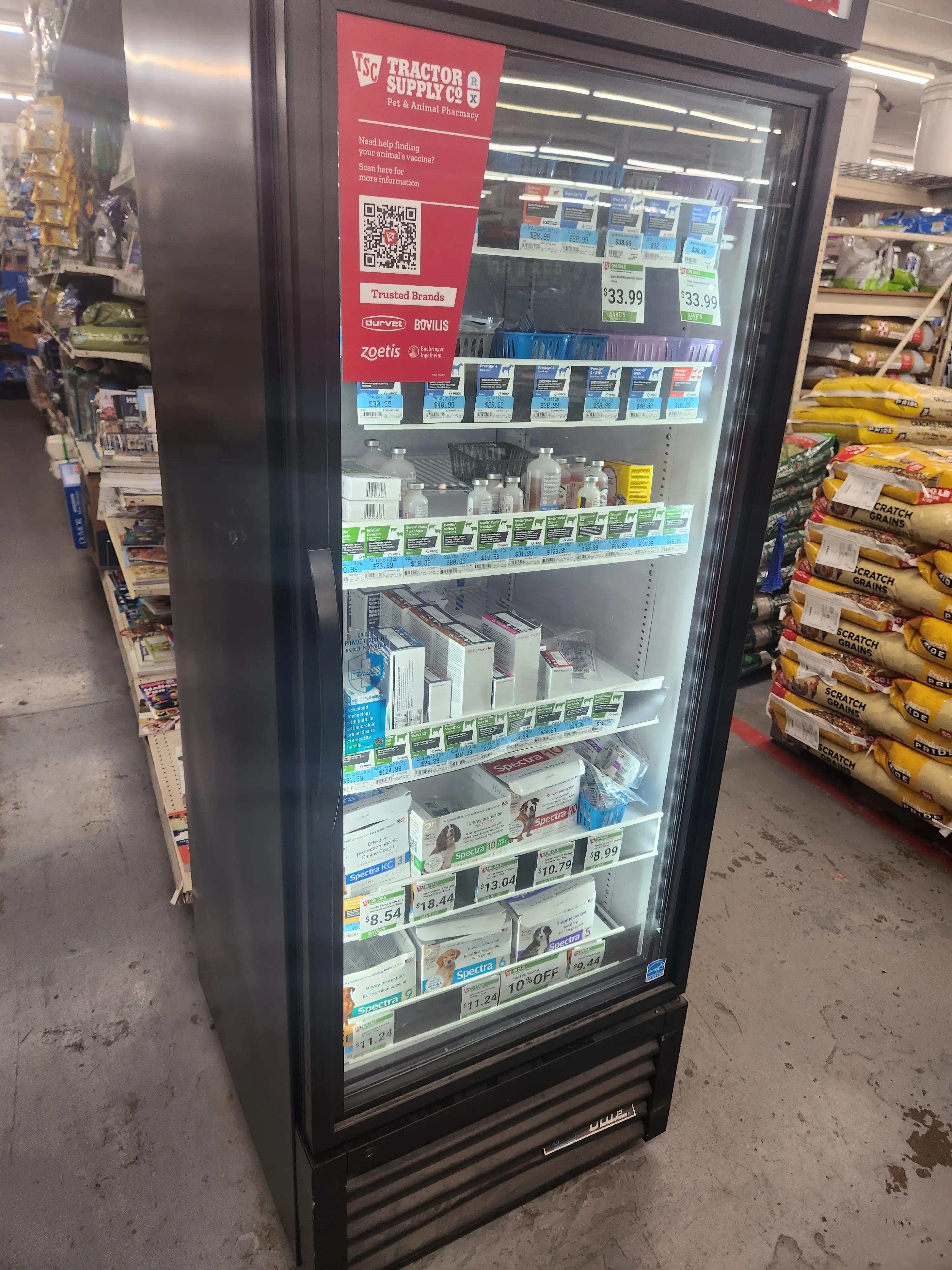 Refrigerated display at Tractor Supply Co. featuring pet vaccines and medications, including Spectra vaccines, with a sign for the Pet & Animal Pharmacy and a visible QR code for more information.