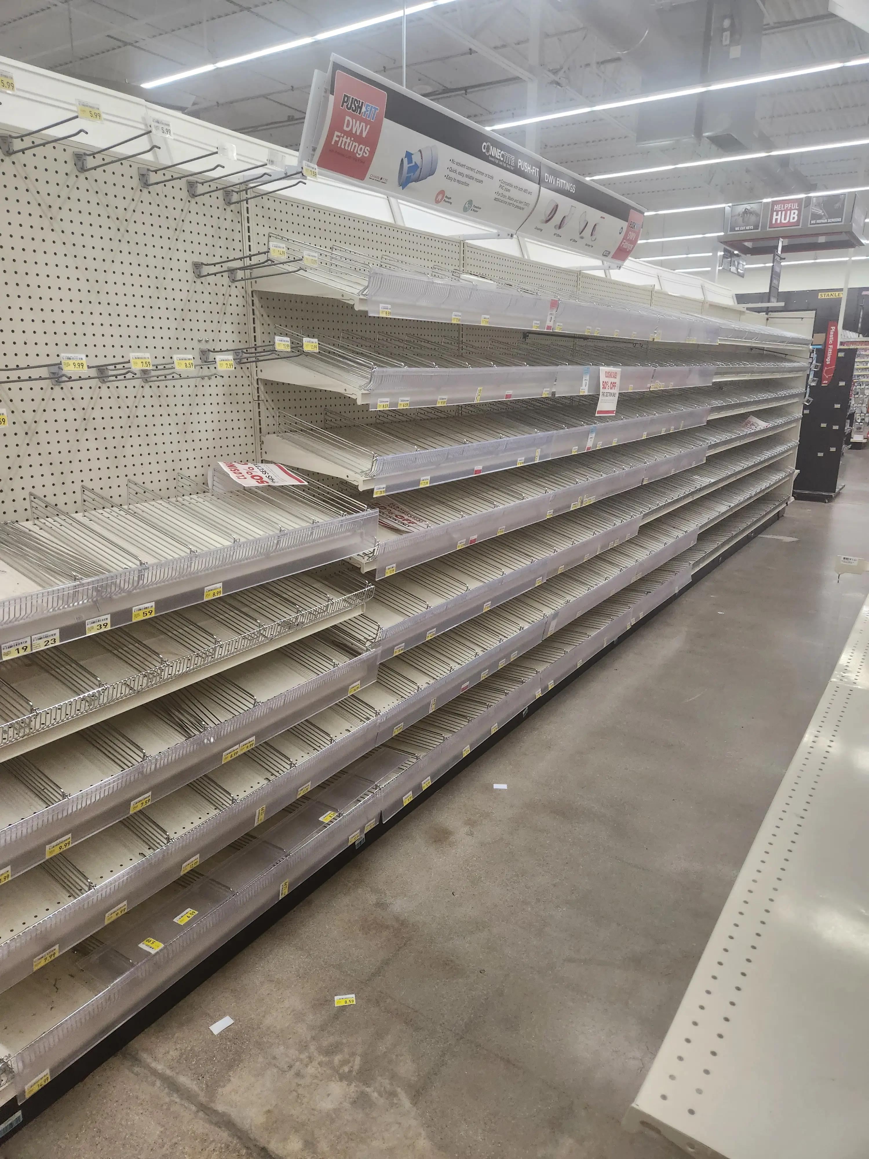 Empty store shelves with signs for DWV fittings and various prices, indicating a closing sale with 50% off. The shelves are mostly bare, suggesting a clearance or end of stock.